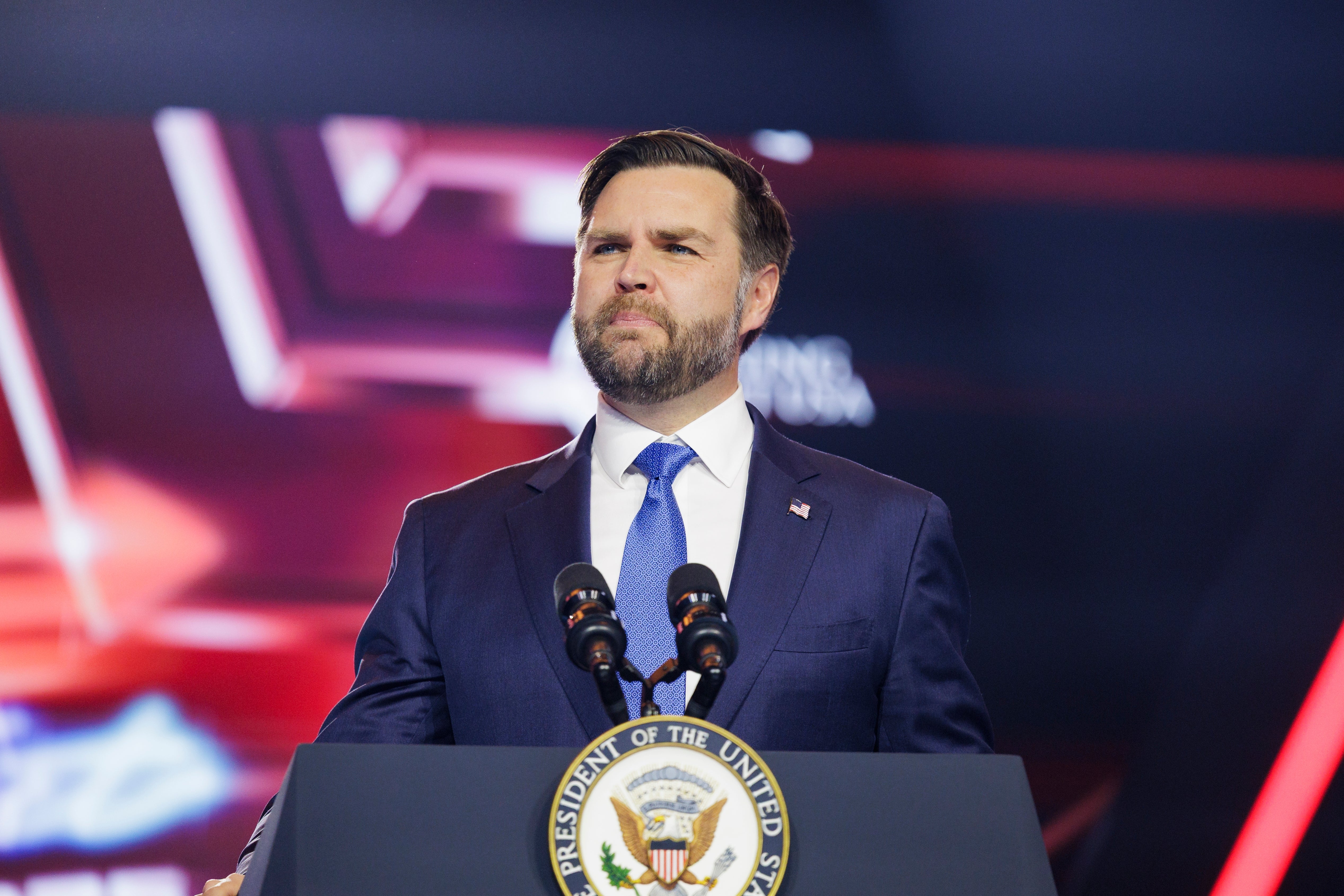 A antheral   successful  a suit   and necktie  stands speaking astatine  a podium with microphones, looking determined
