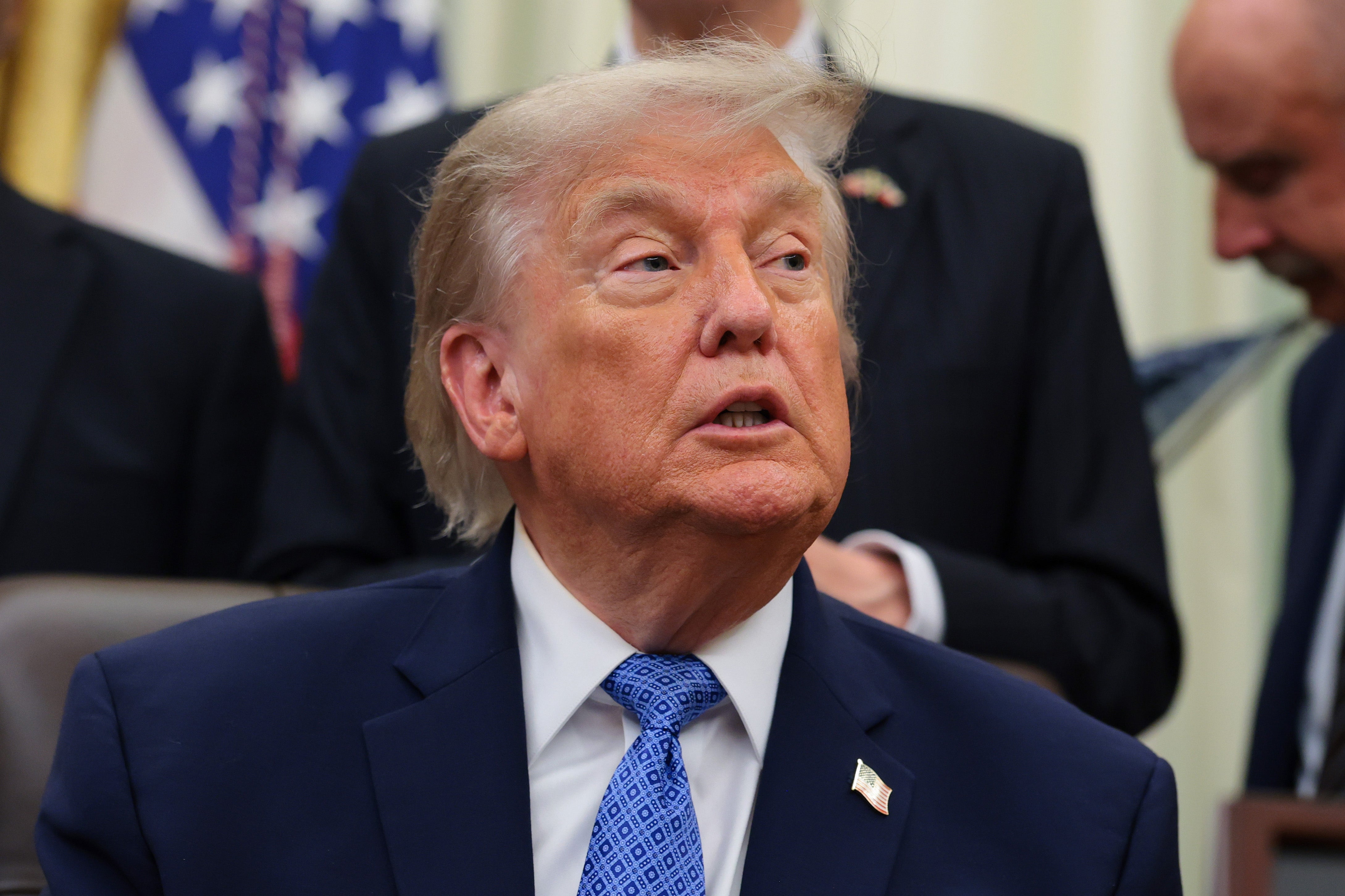 A idiosyncratic   successful  a suit   and necktie  is seated indoors, looking to the broadside  during a ceremonial  lawsuit   with radical   successful  the background
