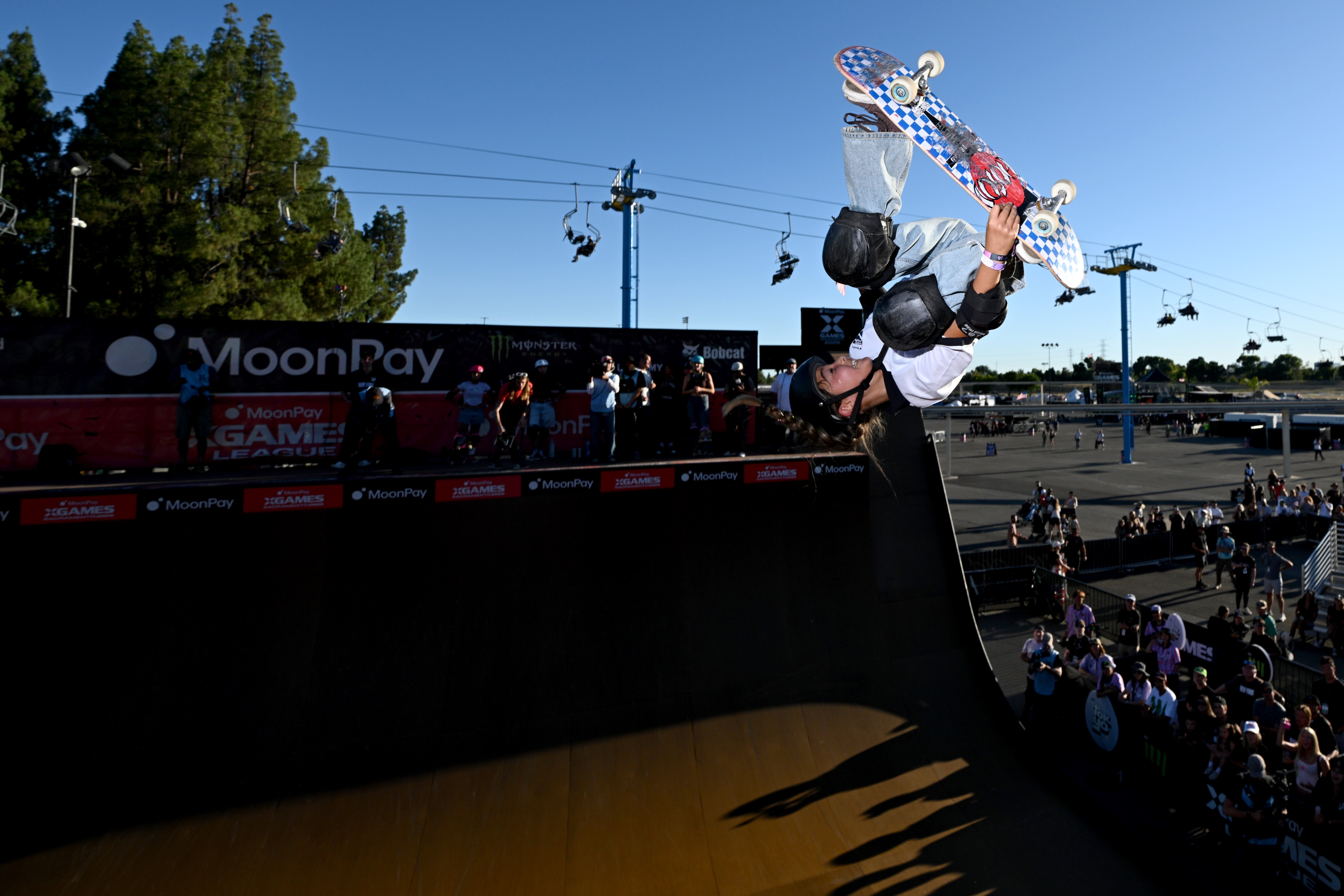 A skateboarder performs an aerial instrumentality   disconnected  a ramp astatine  an outdoor skatepark event, observed by a assemblage  below