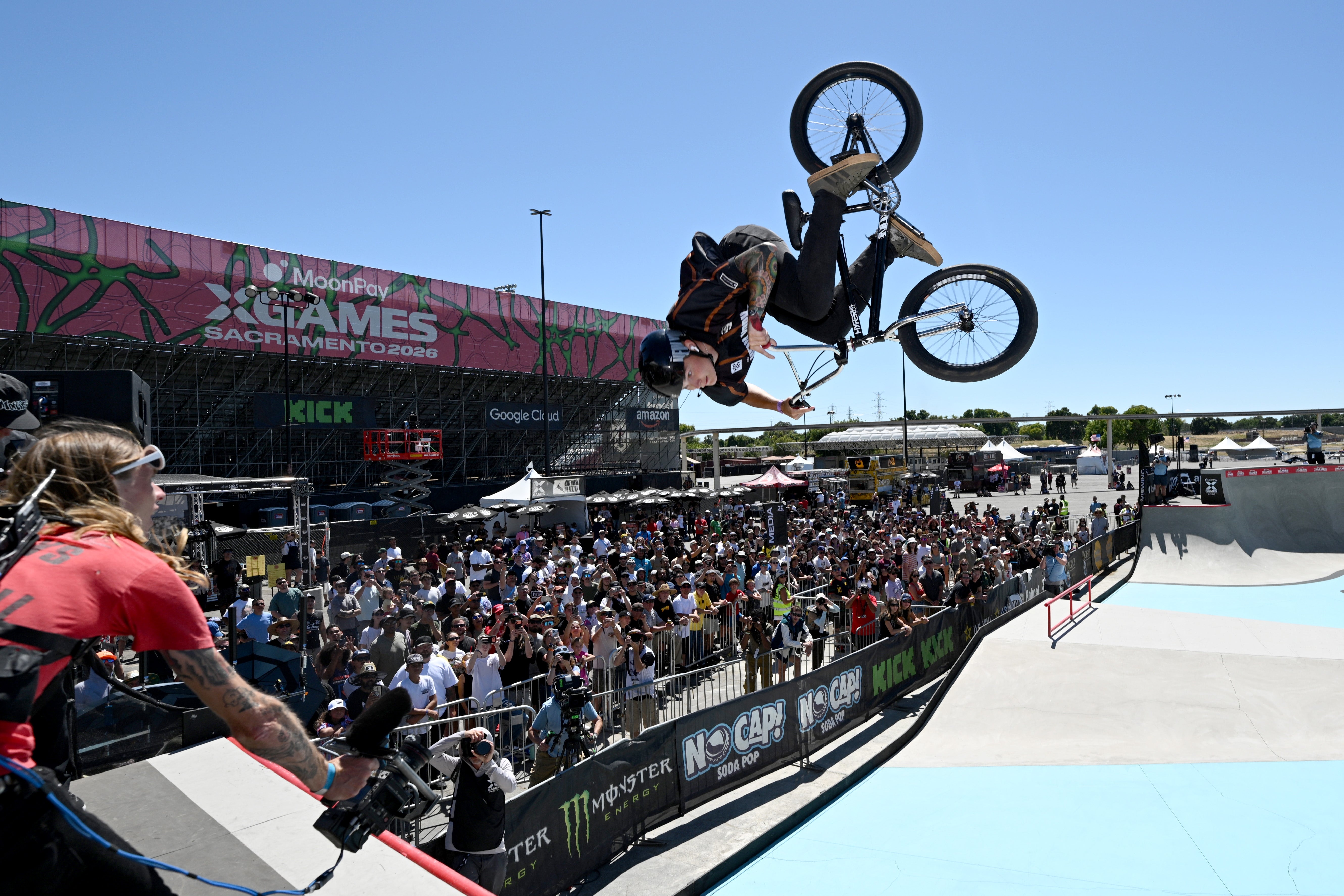 BMX rider performs an inverted aerial instrumentality   astatine  a skatepark lawsuit   successful  beforehand   of a ample  crowd, with lawsuit   signage successful  the background