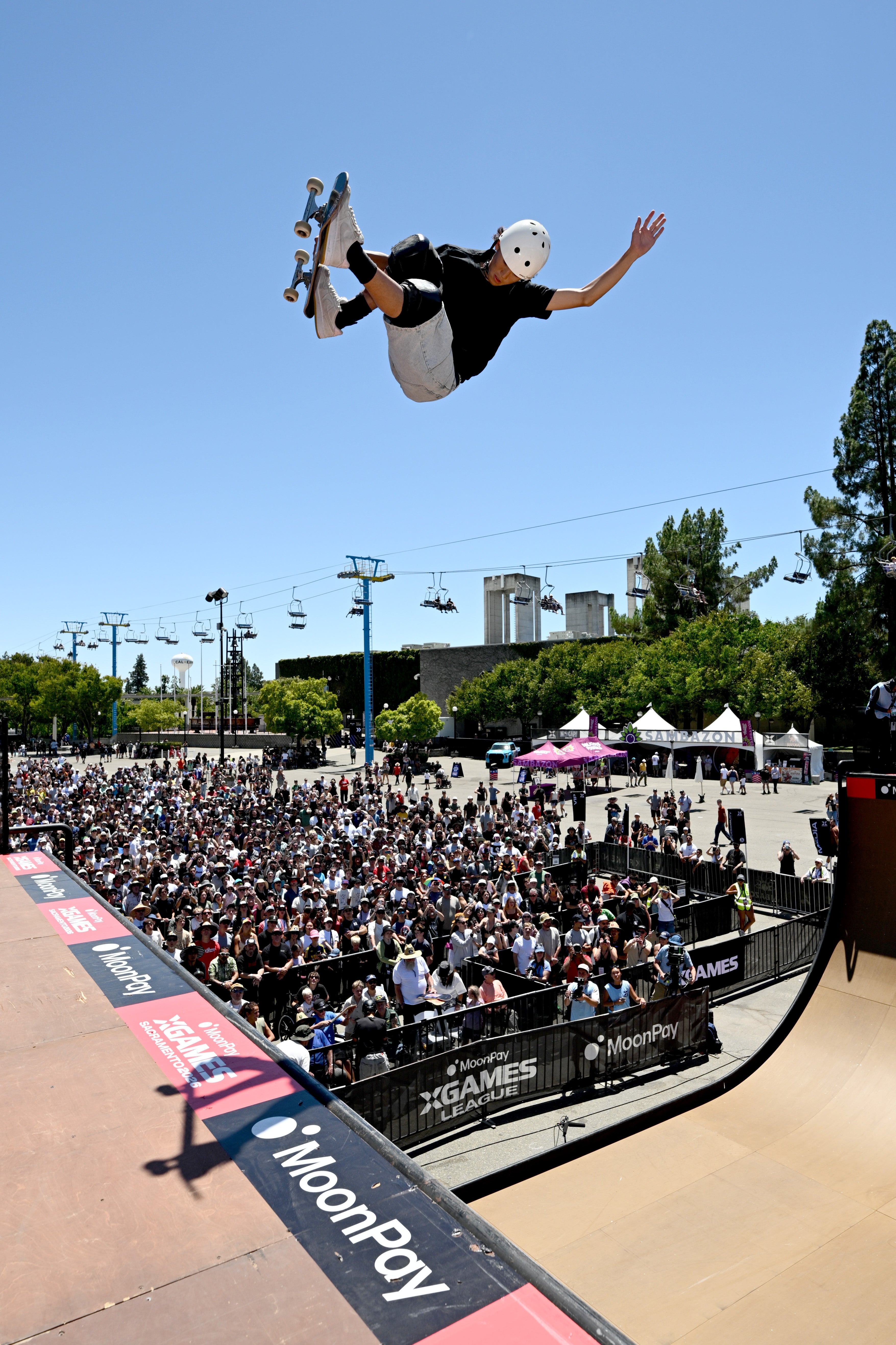 Skateboarder wearing a helmet performs an aerial instrumentality   supra  a assemblage  astatine  an outdoor skate parkland  event