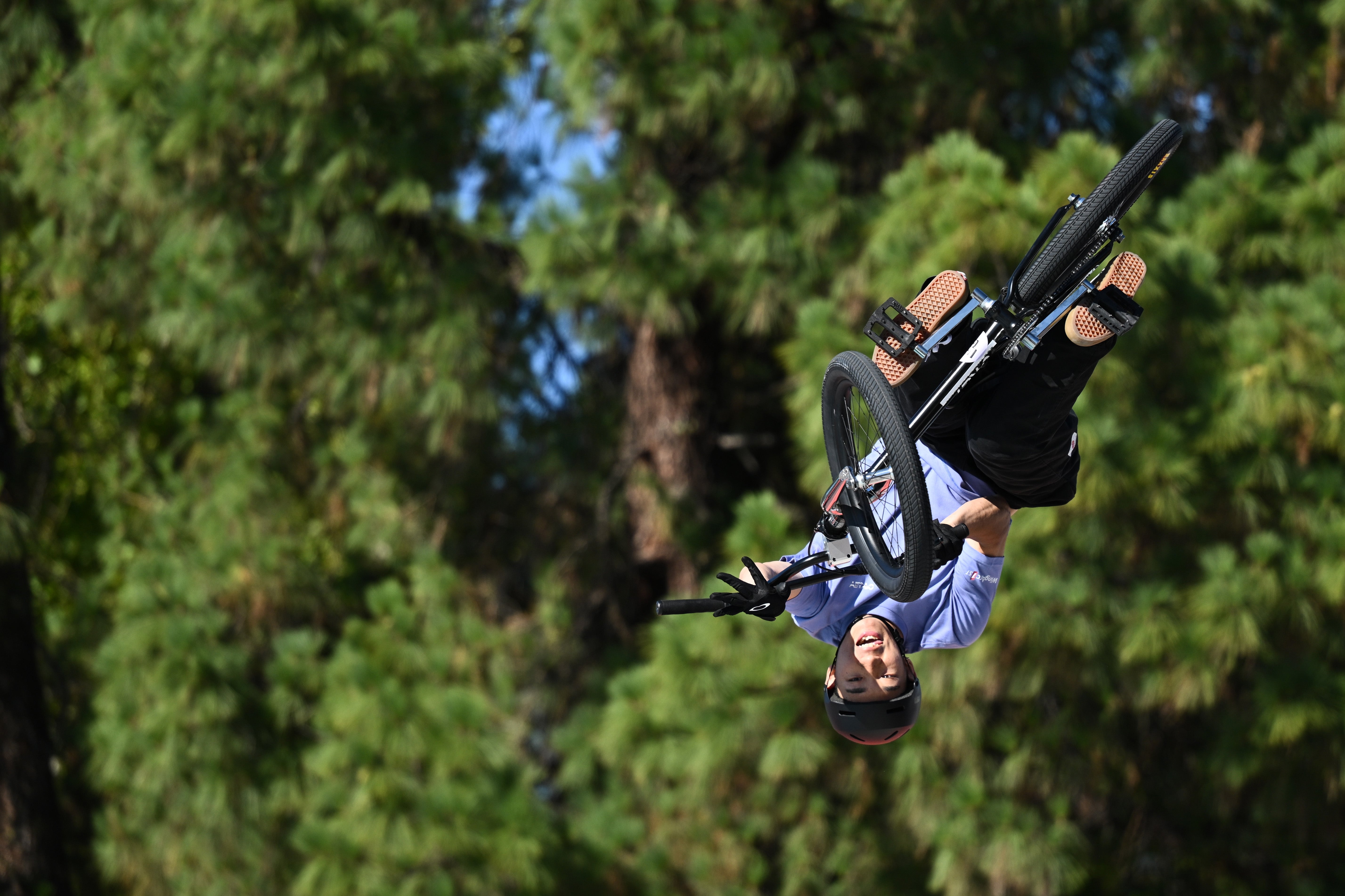 Person performing a high-flying BMX stunt, mid-air, against a backdrop of trees