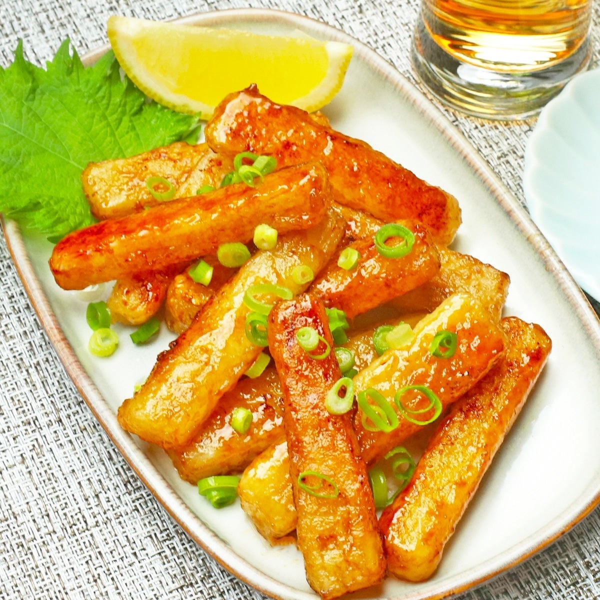 長芋のバタポン焼きが皿に盛られ、ネギとレモンが添えられた料理。飲み物が近くに置かれている。