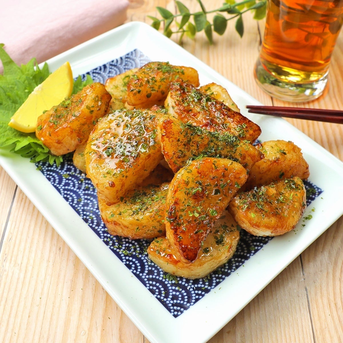 皿に盛られた長芋のバターしょうゆ焼き。レモンとハーブが添えられている。背景には飲み物。