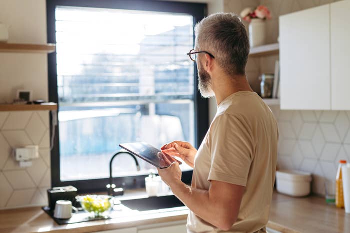 Man successful  room  utilizing tablet successful  sunlight, lasting  by window