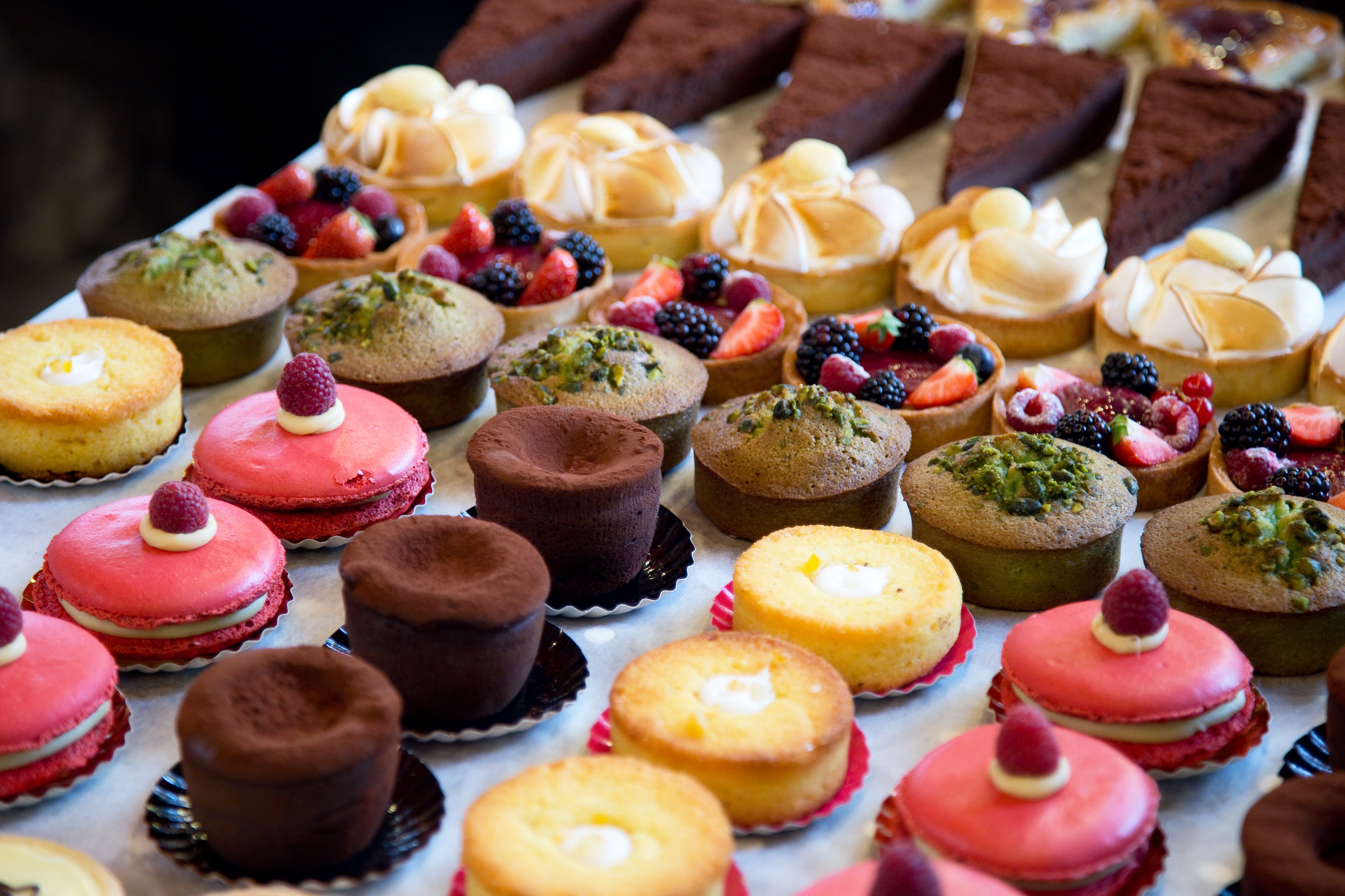 Assorted pastries and desserts arranged connected a table, featuring berry-topped tarts, cocoa cakes, and cream-filled treats
