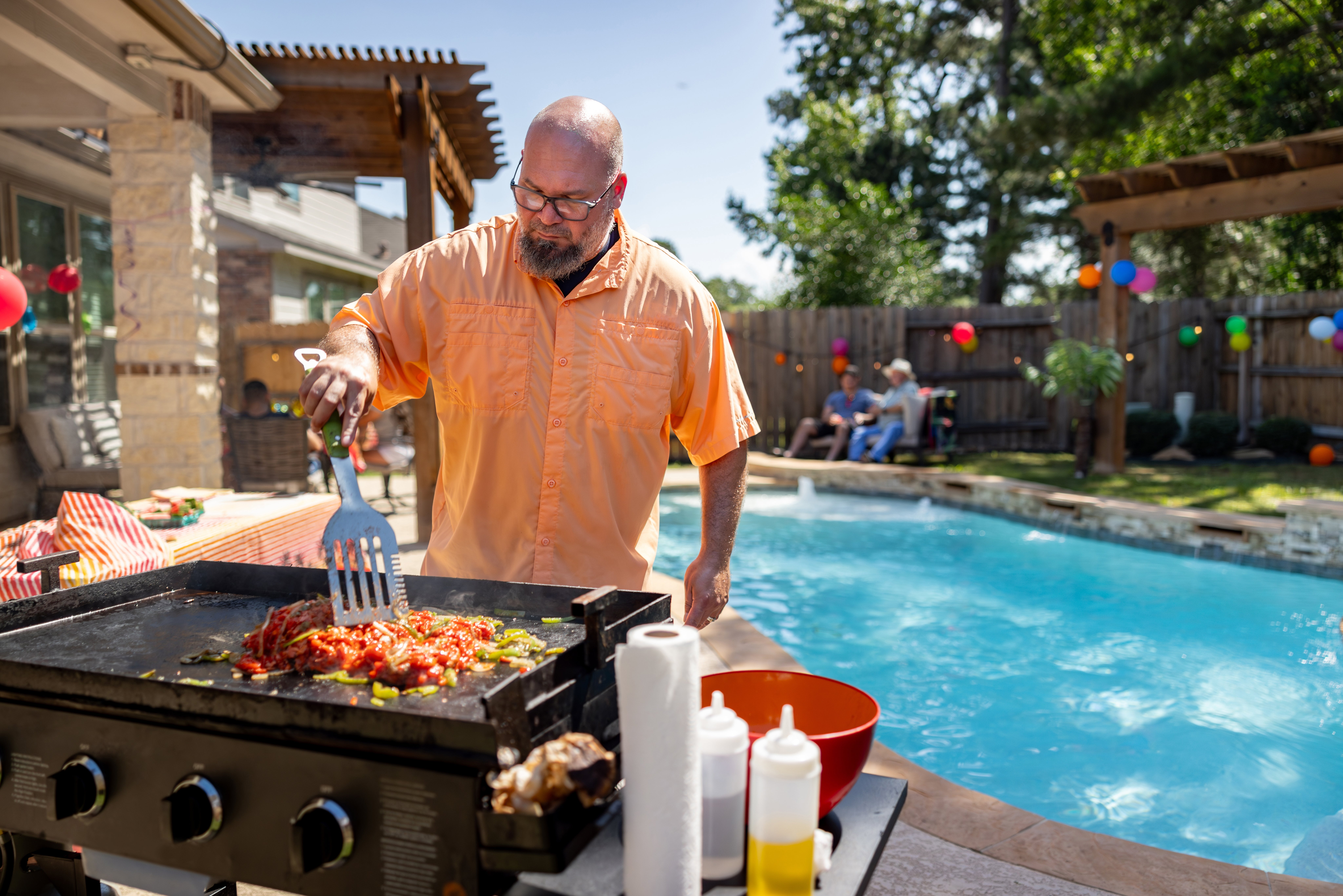 Man cooking connected a grill by a pool, wearing casual summertime attire; a relaxed poolside gathering is successful the background