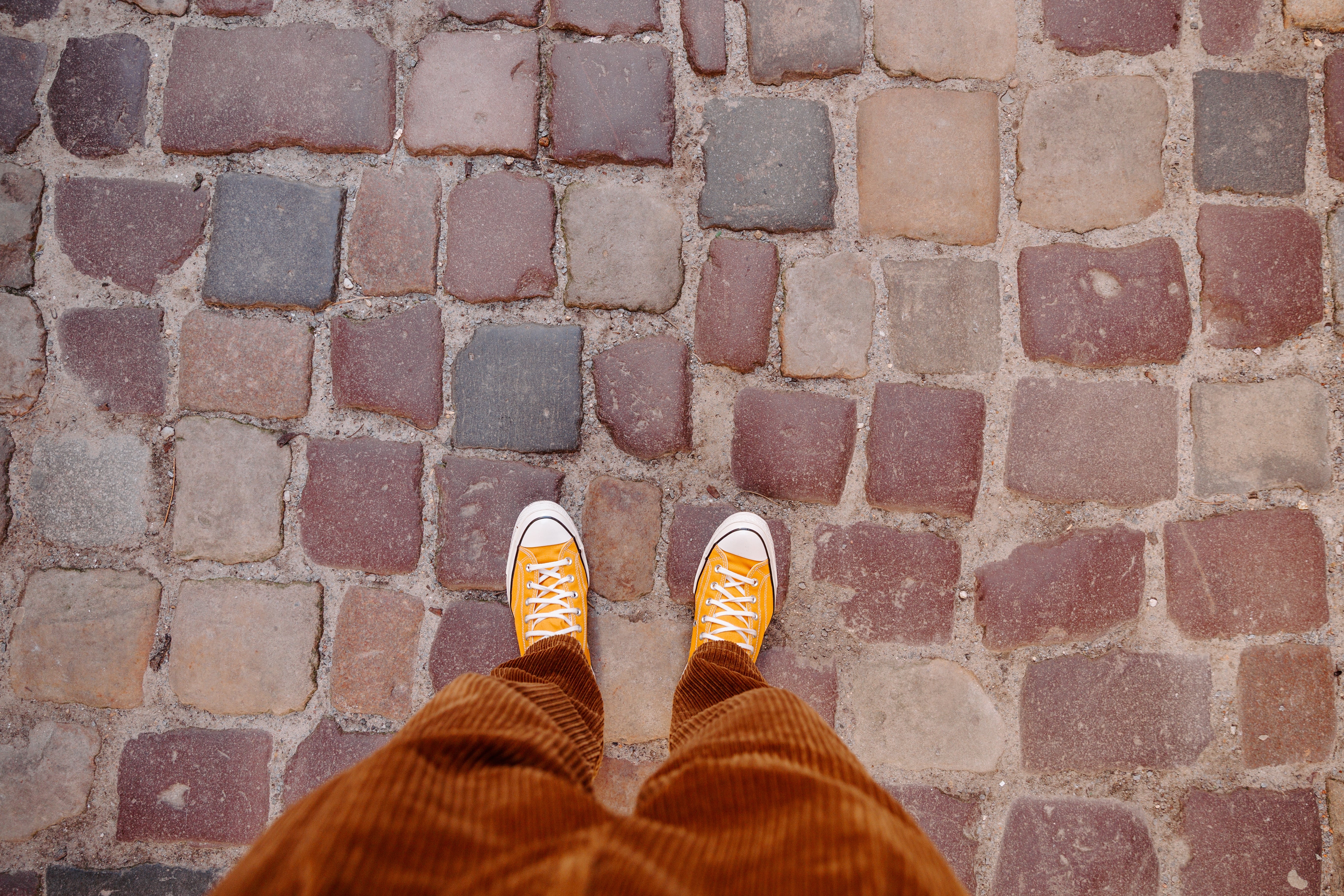 Feet successful  orangish  sneakers connected  a cobblestone path, viewed from above. The representation  conveys a consciousness   of casual stroll and freedom