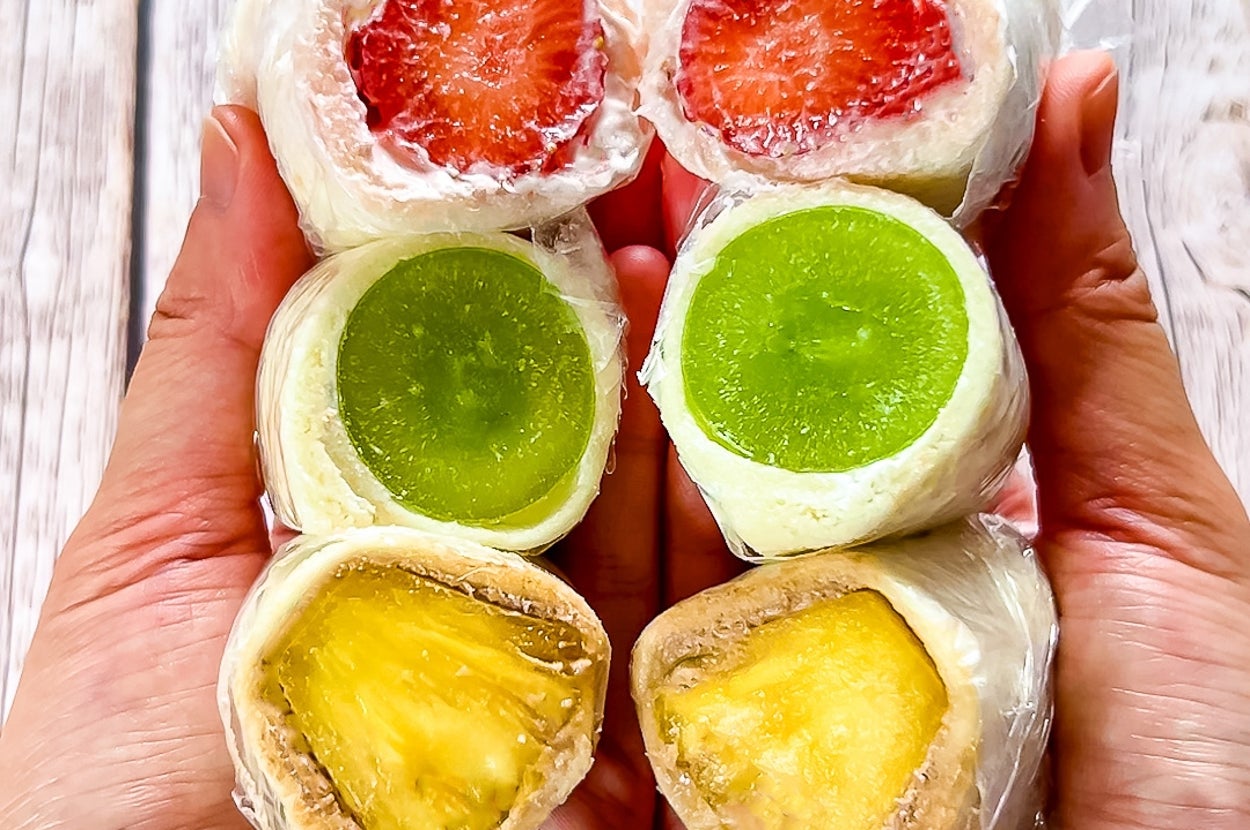 手に持たれた3種のフルーツサンドイッチ。上からいちご、マスカット、パイナップルの順に並んでいる。