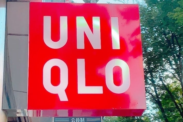 ユニクロの赤い店頭看板。店名が大きく表示されている。背景に緑の木々が見える。