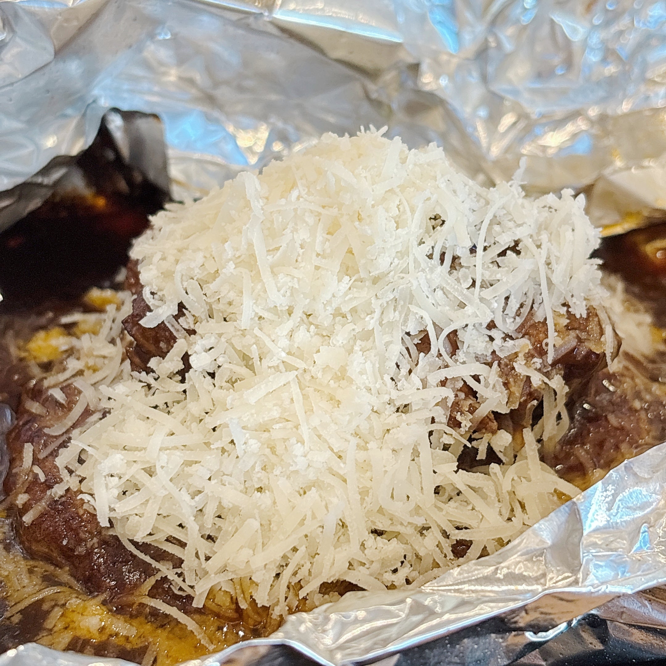 ココスの「山盛りチーズの濃厚ビーフシチュー包み焼きハンバーグ145g」アルミホイルに包まれたハンバーグの上に、たっぷりのチーズがのせられている様子。