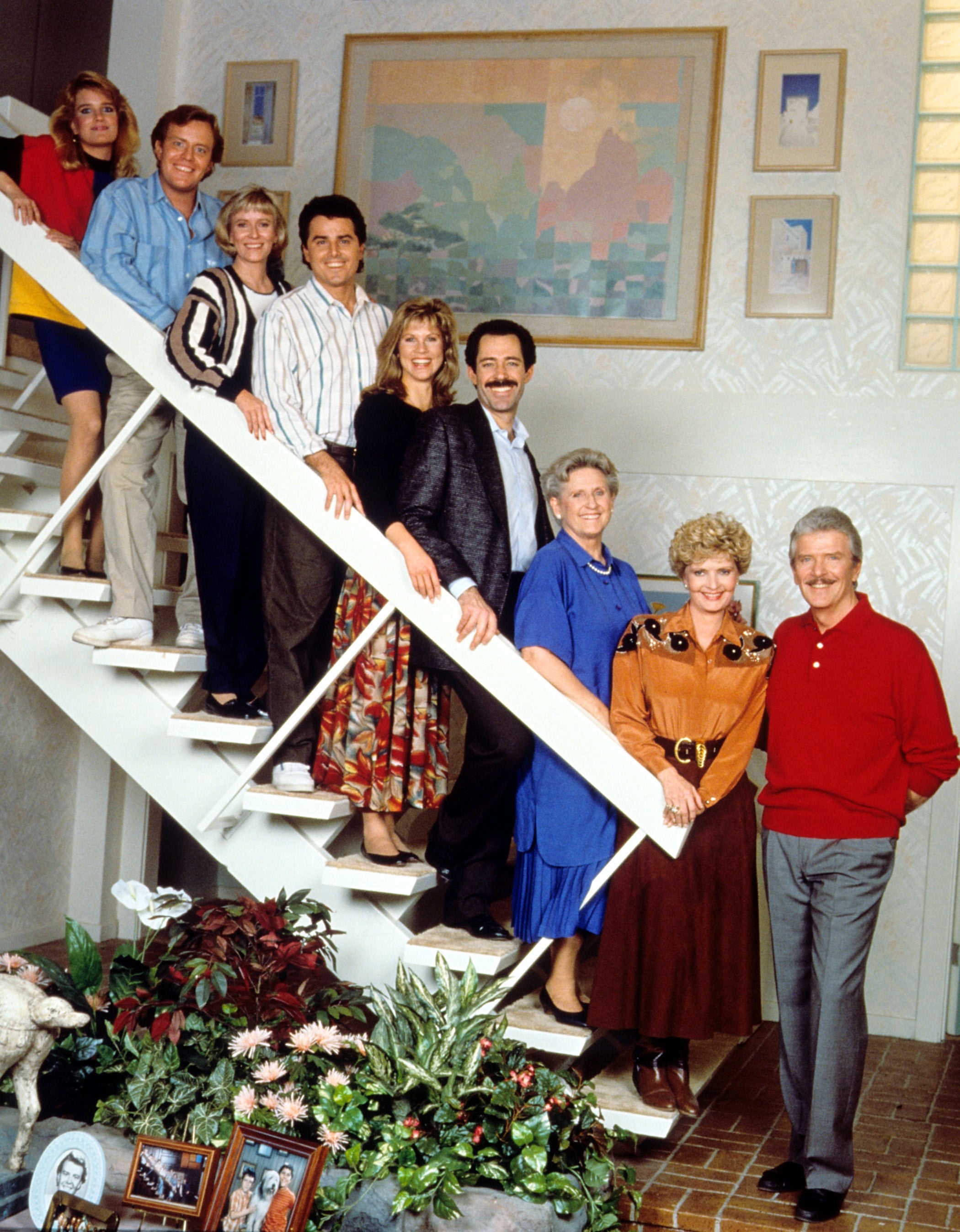 A radical  of radical   airs  connected  indoor stairs, dressed successful  1980s attire, including sweaters, collared shirts, a floral skirt, and a bluish  dress