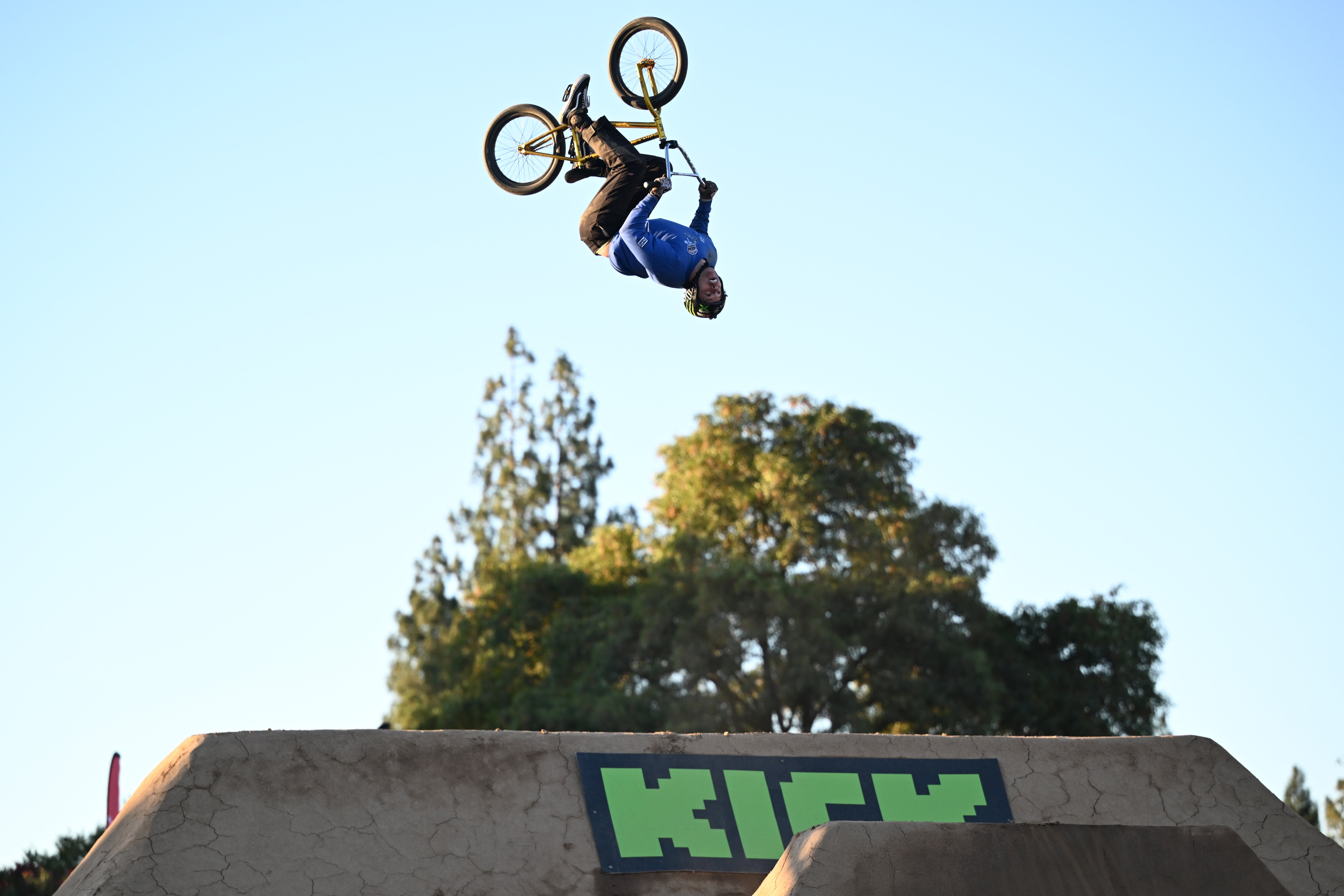 A BMX biker performs an upside-down aerial stunt disconnected  a ungraded  ramp against a wide   sky. Trees are disposable   successful  the background