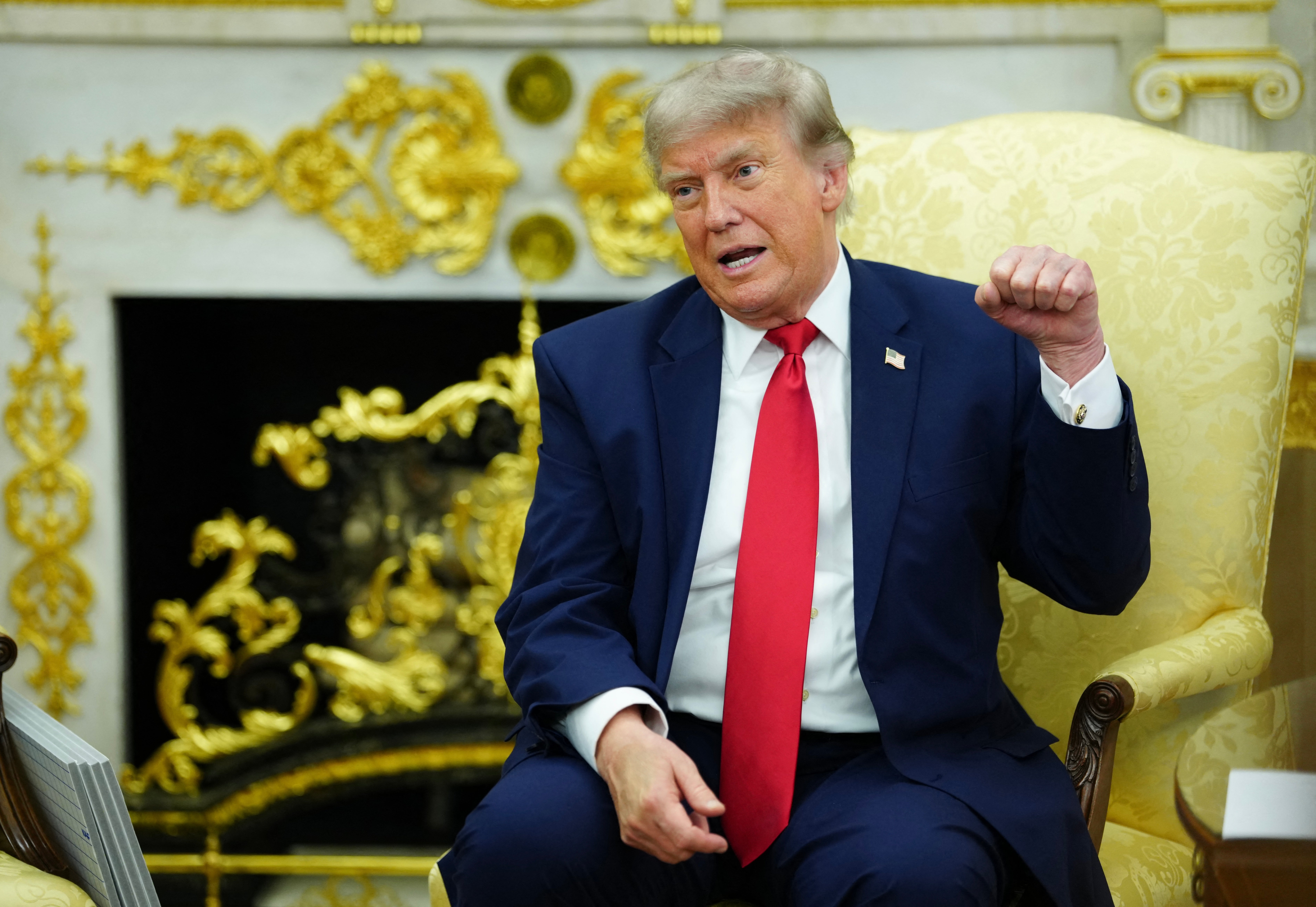 A idiosyncratic successful a suit and necktie sits successful an ornate room, gesturing portion speaking
