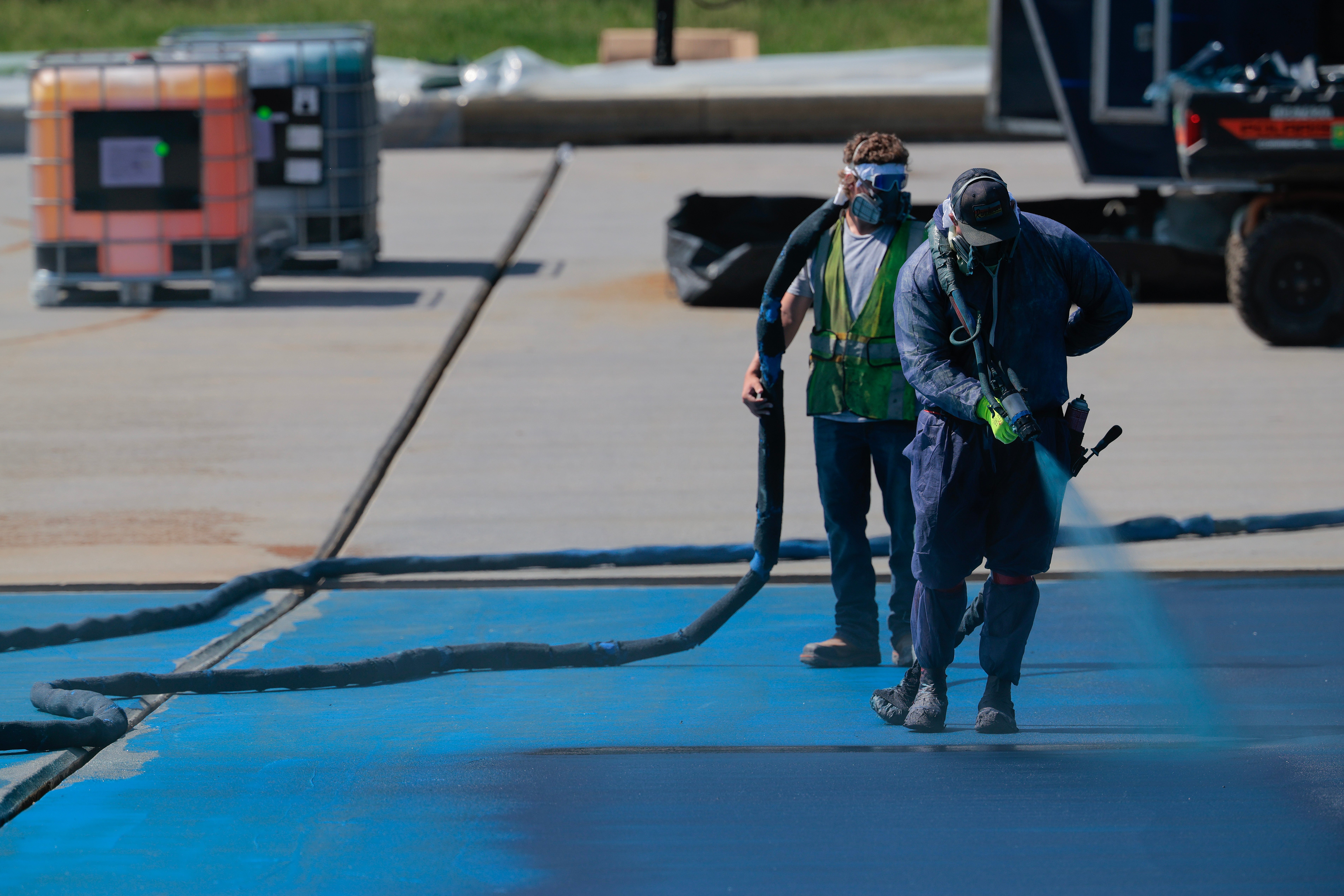 Two workers spray a aboveground outdoors, 1 utilizing a ample hose. Both deterioration information gear, including masks and protective clothing