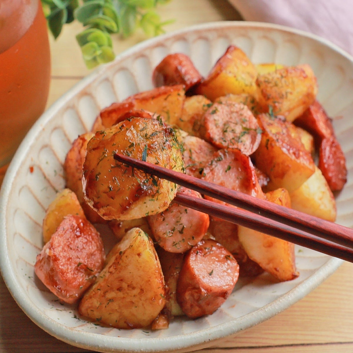 皿に盛られた焼きじゃがいもと魚肉ソーセージの一口サイズ料理。箸で一つを持ち上げている。