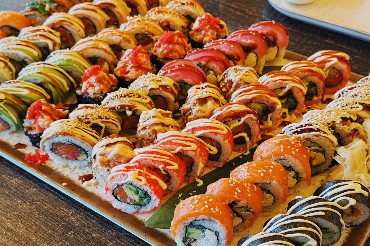 A large, colorful platter of assorted sushi rolls, featuring various toppings and fillings, displayed on a textured surface