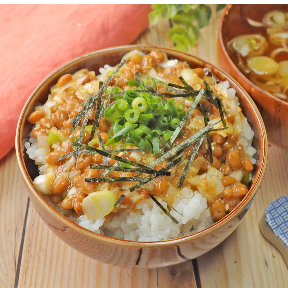 納豆ご飯が盛られた器。刻みネギと海苔がトッピングされている。横には味噌汁が置かれている。