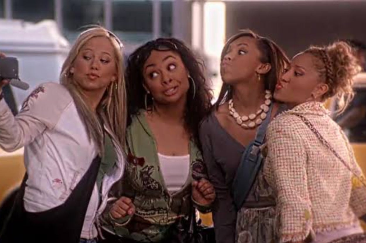 Four women pose playfully for a selfie. Three wear casual jackets and one is in a textured coat with styled hair