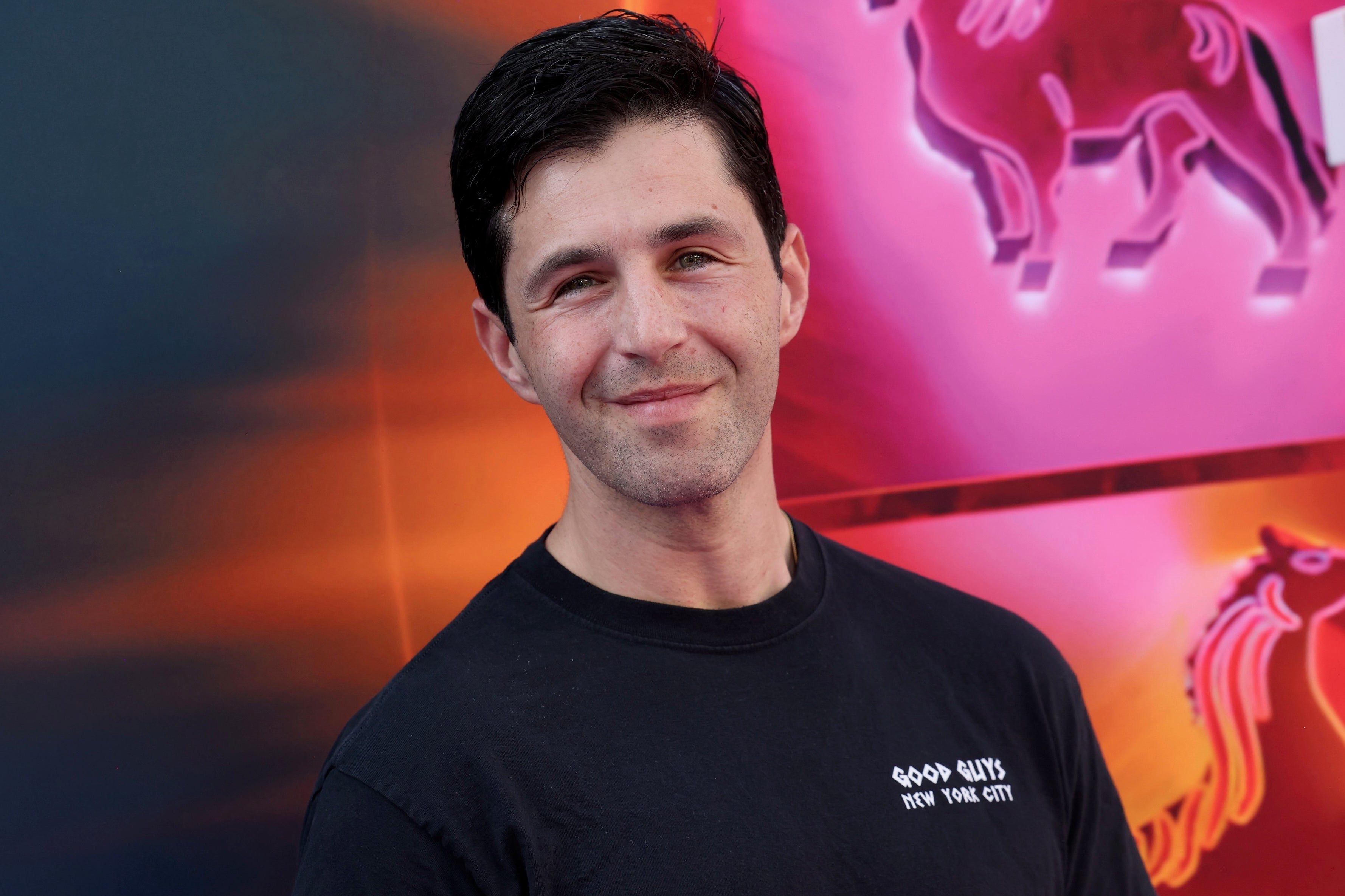 Man in a casual black t-shirt with "Good Guys New York City" stands in front of a colorful background featuring neon animal designs