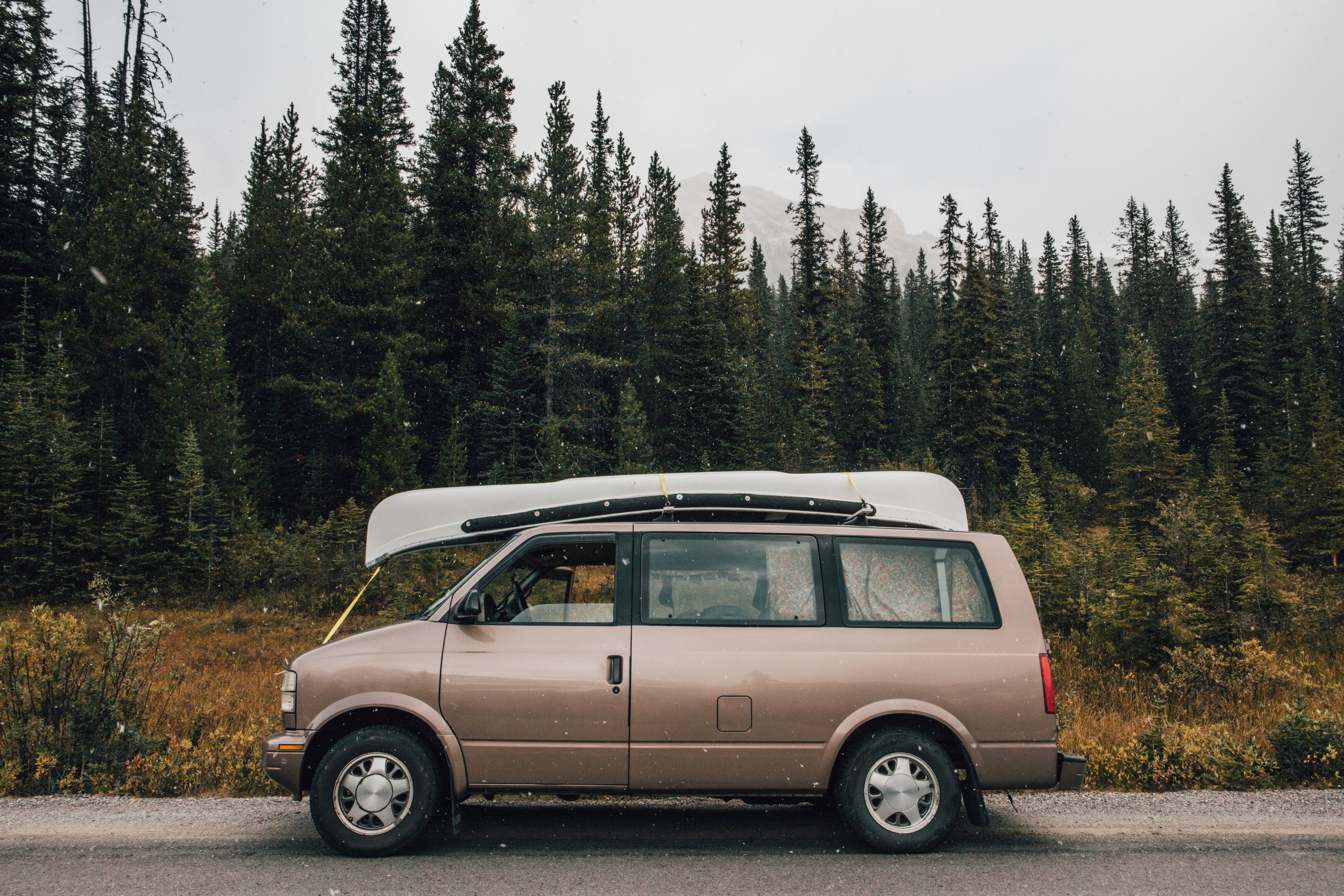 Van with a canoe connected apical parked by a forested road. Conifer trees successful the background