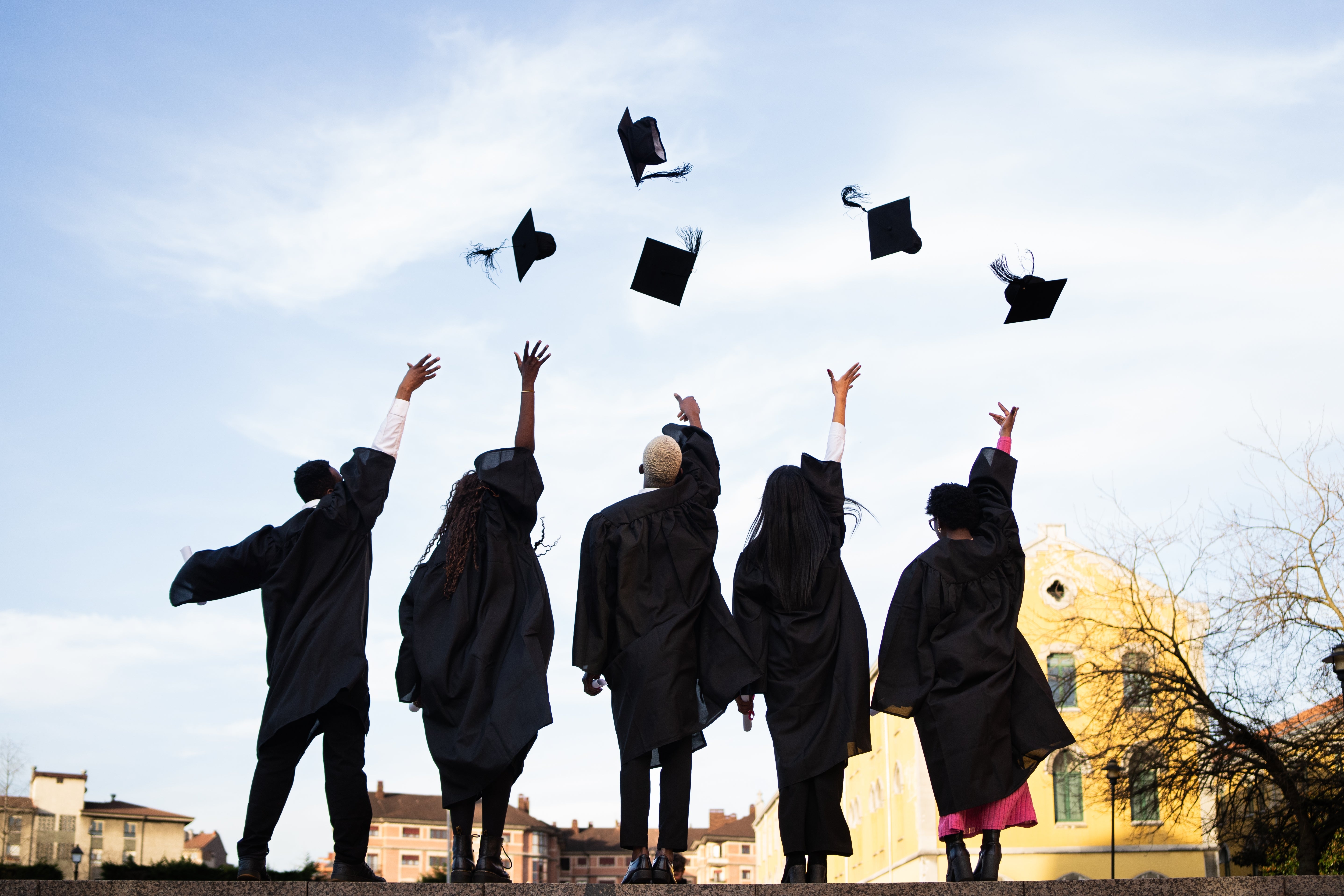 Graduates successful caps and gowns joyfully propulsion their caps into the air, celebrating their accomplishment outdoors