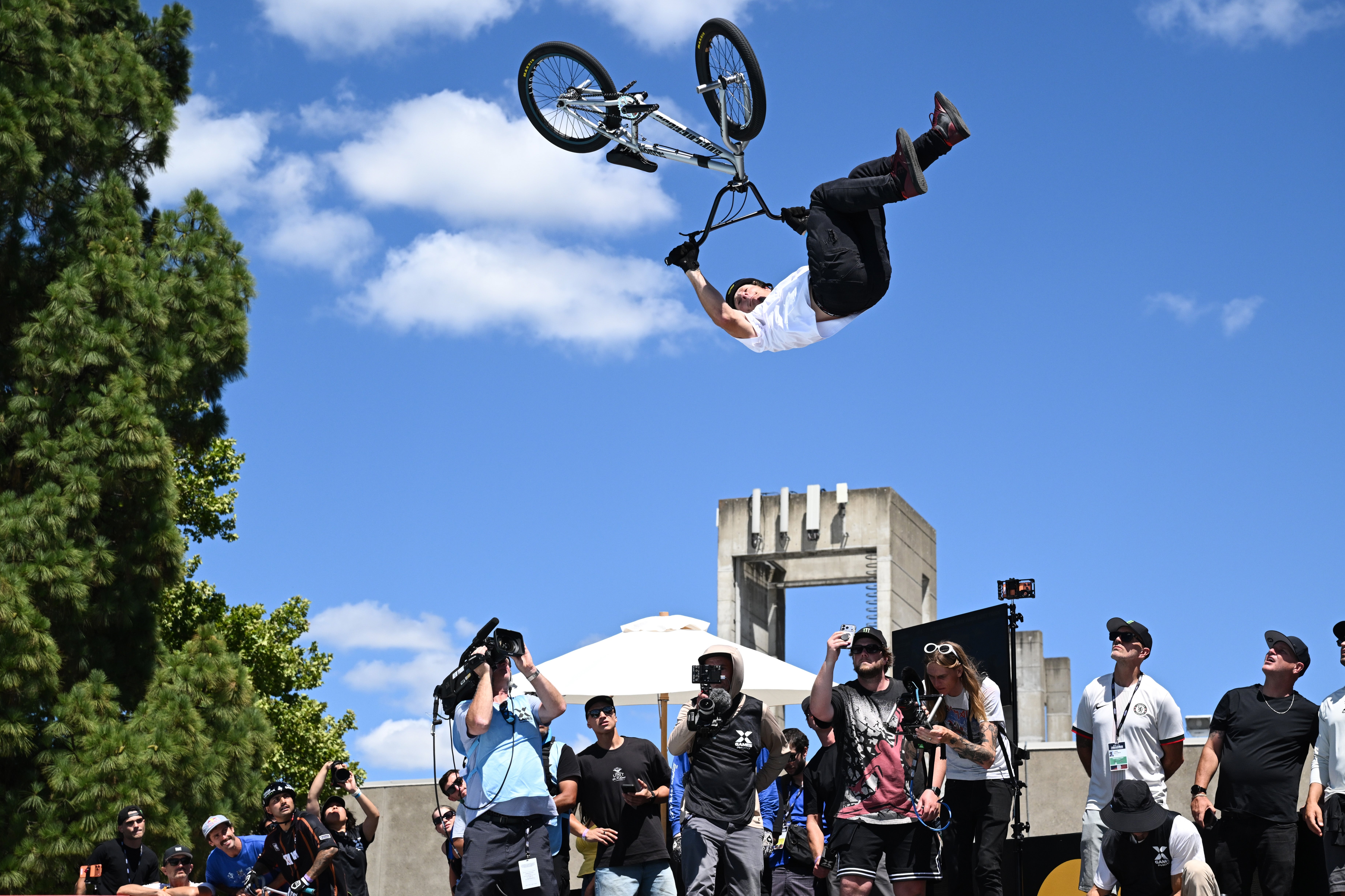 BMX rider performs an aerial instrumentality   mid-air astatine  an outdoor sports event, surrounded by photographers and spectators