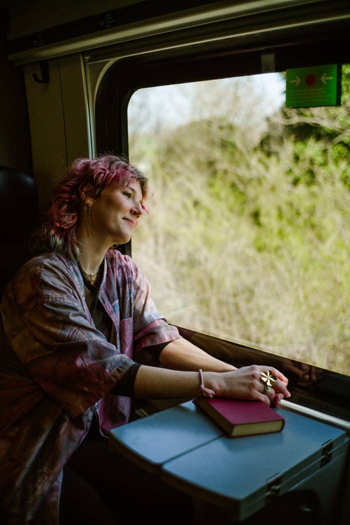 Person with abbreviated  hairsbreadth  wearing casual attire, smiling portion    gazing retired  a bid     window. A publication  rests connected  the array  successful  beforehand   of them
