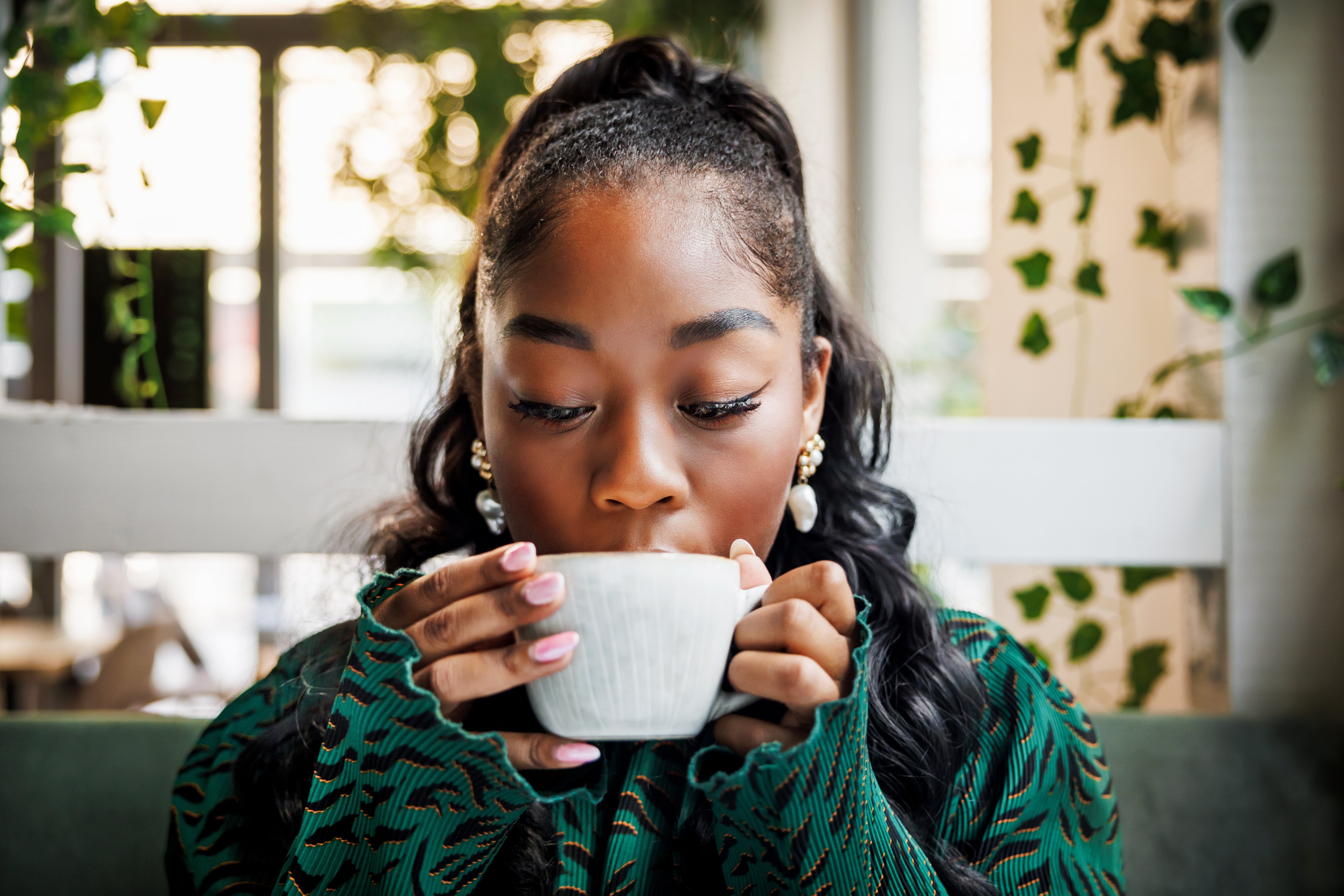 Person drinking from a cupful successful a cozy café mounting with plants successful the background