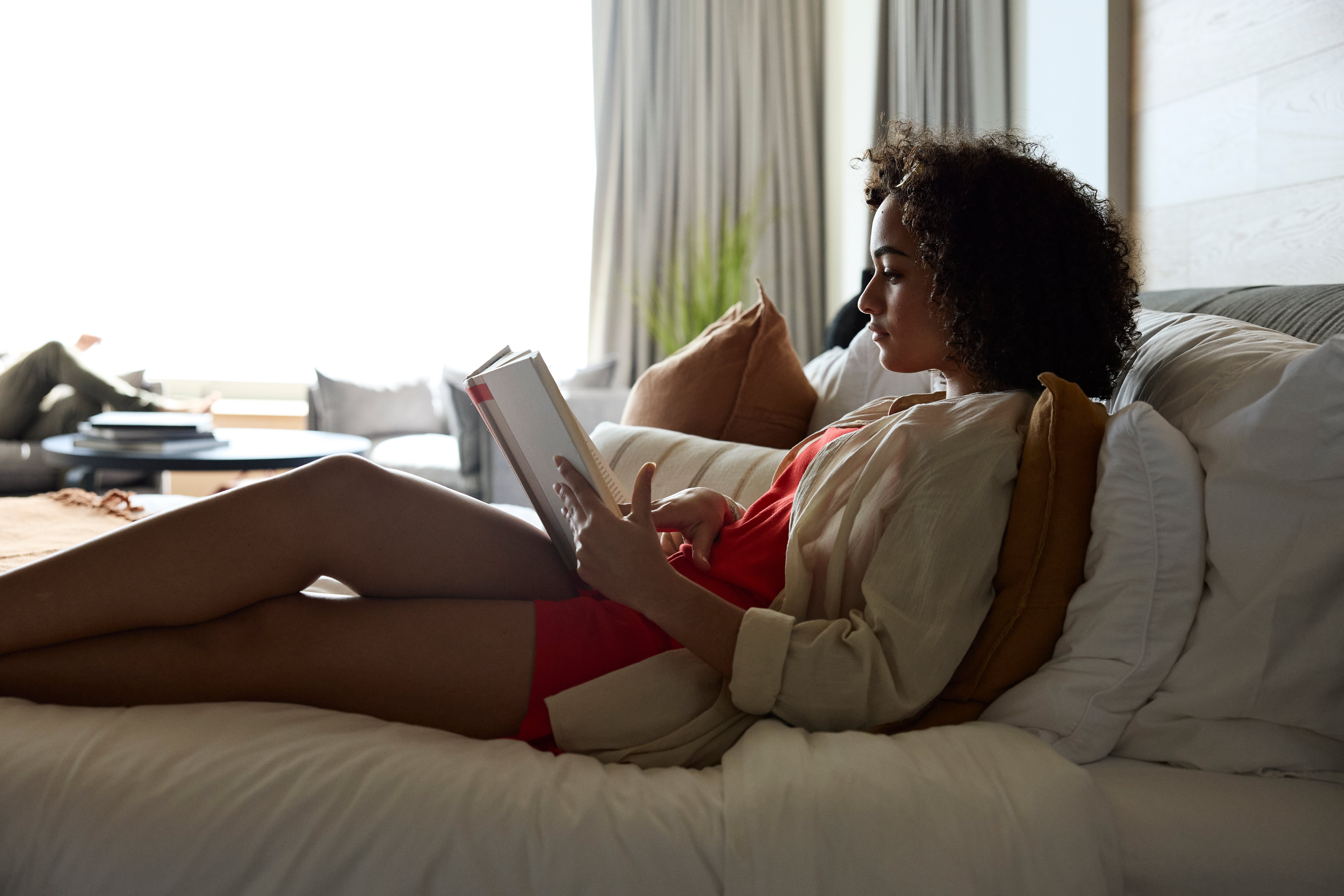 Person lounging connected a furniture portion speechmaking a book, appearing relaxed and absorbed successful their activity