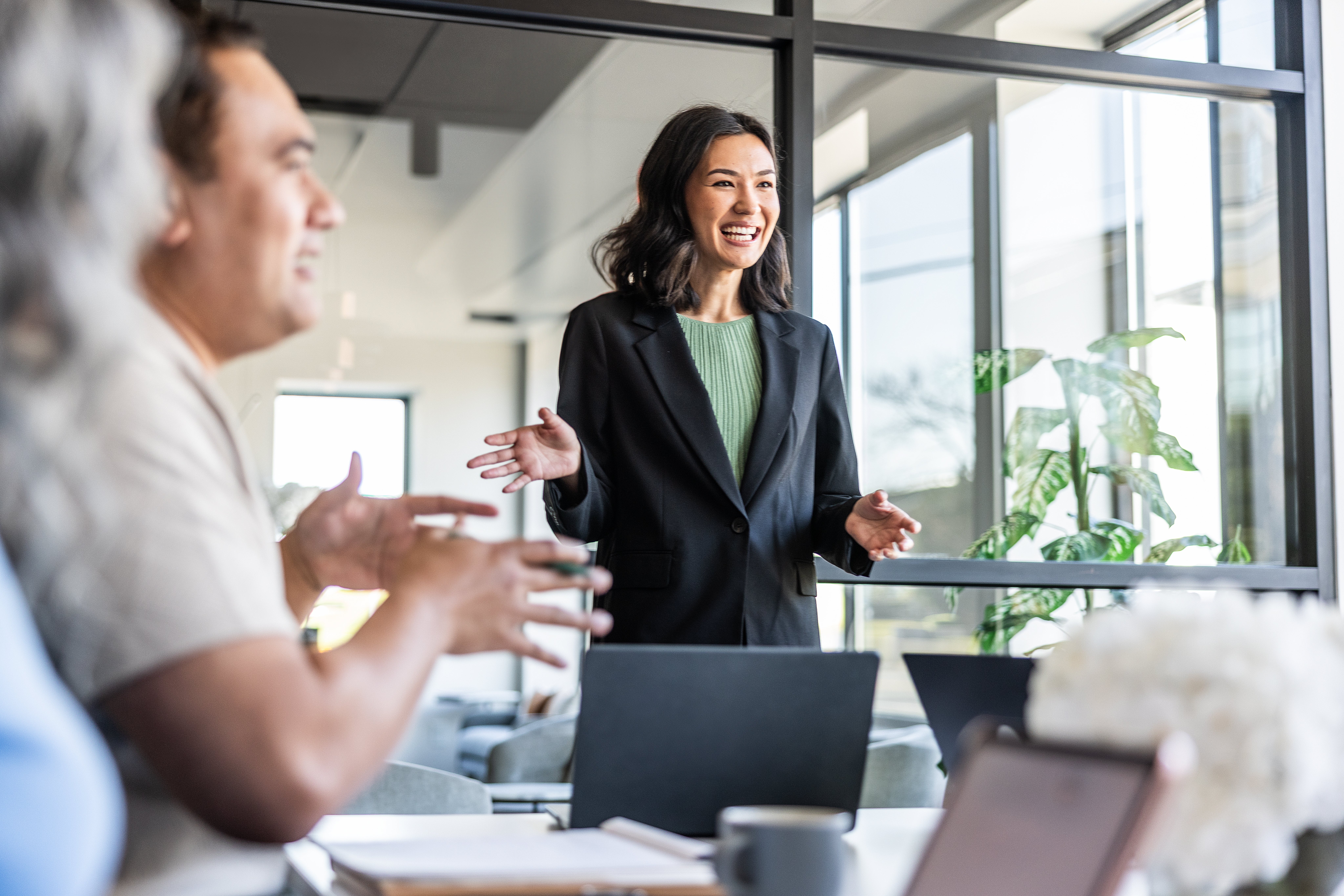 A idiosyncratic successful a concern mounting speaks confidently to colleagues. They are wearing a blazer and smiling, appearing engaged successful the discussion