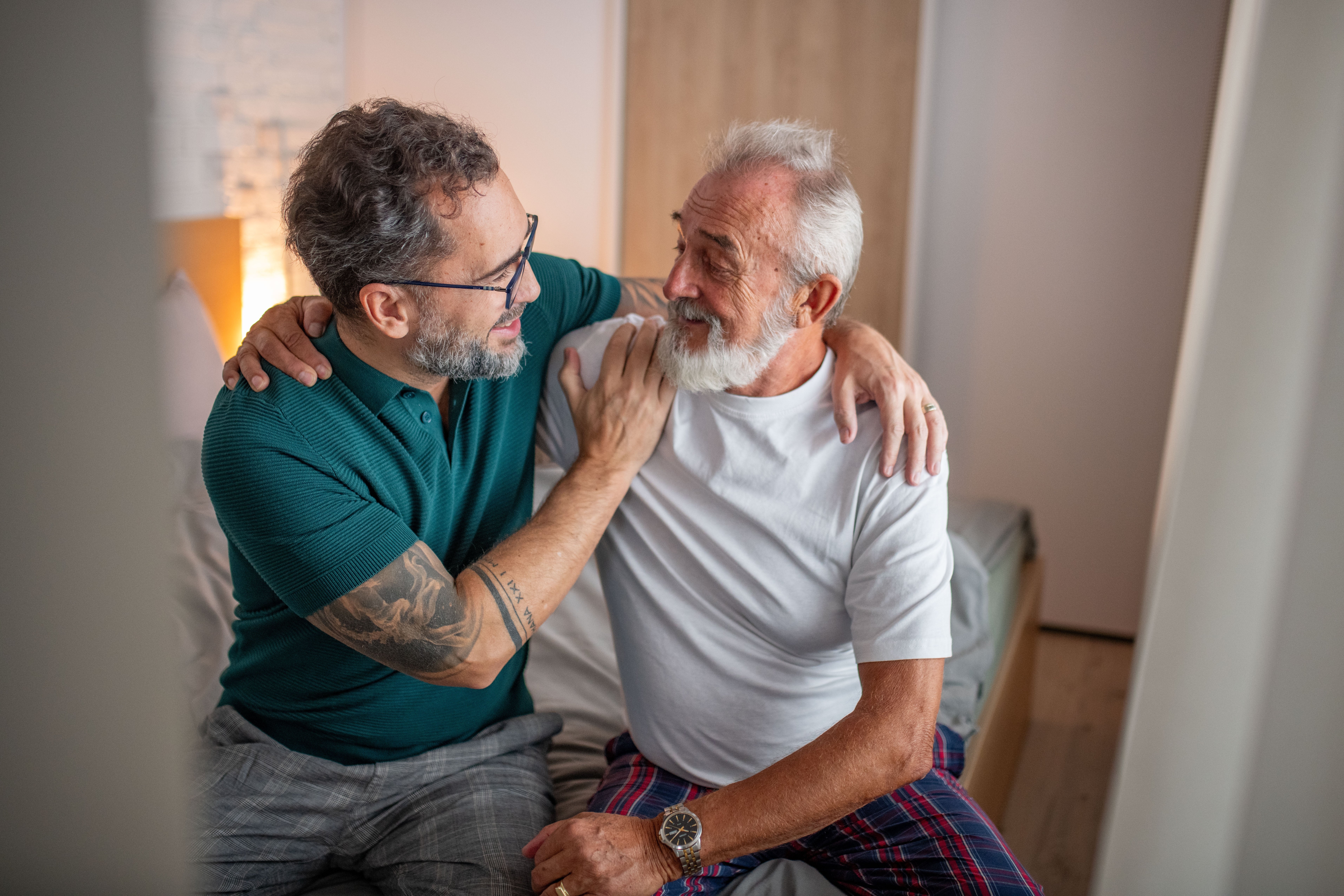 Two older adults sitting connected a bed, smiling and embracing successful a warm, affectionate moment