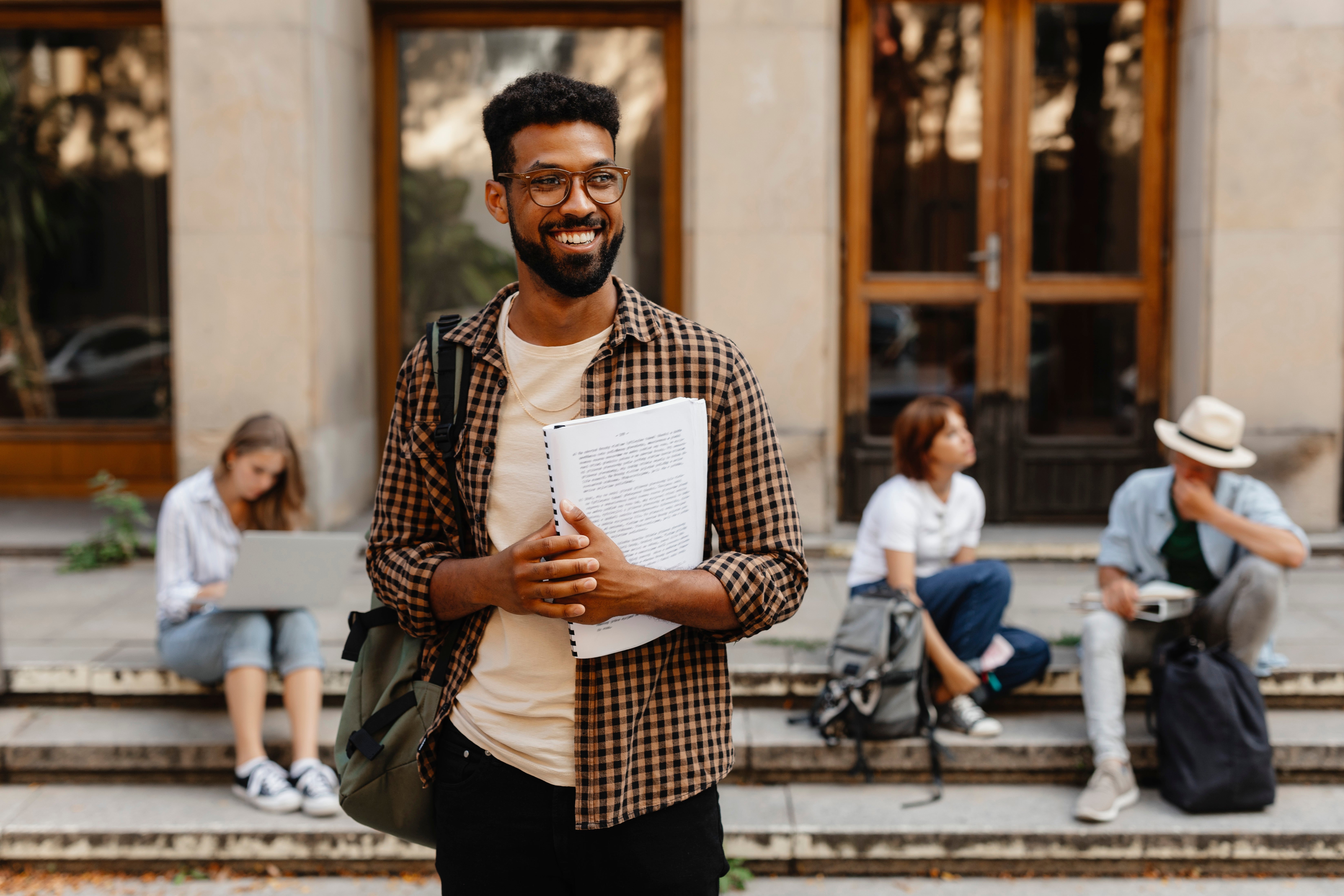 A smiling idiosyncratic holds a notebook, lasting extracurricular connected steps with others sitting successful the background, engaged successful assorted activities