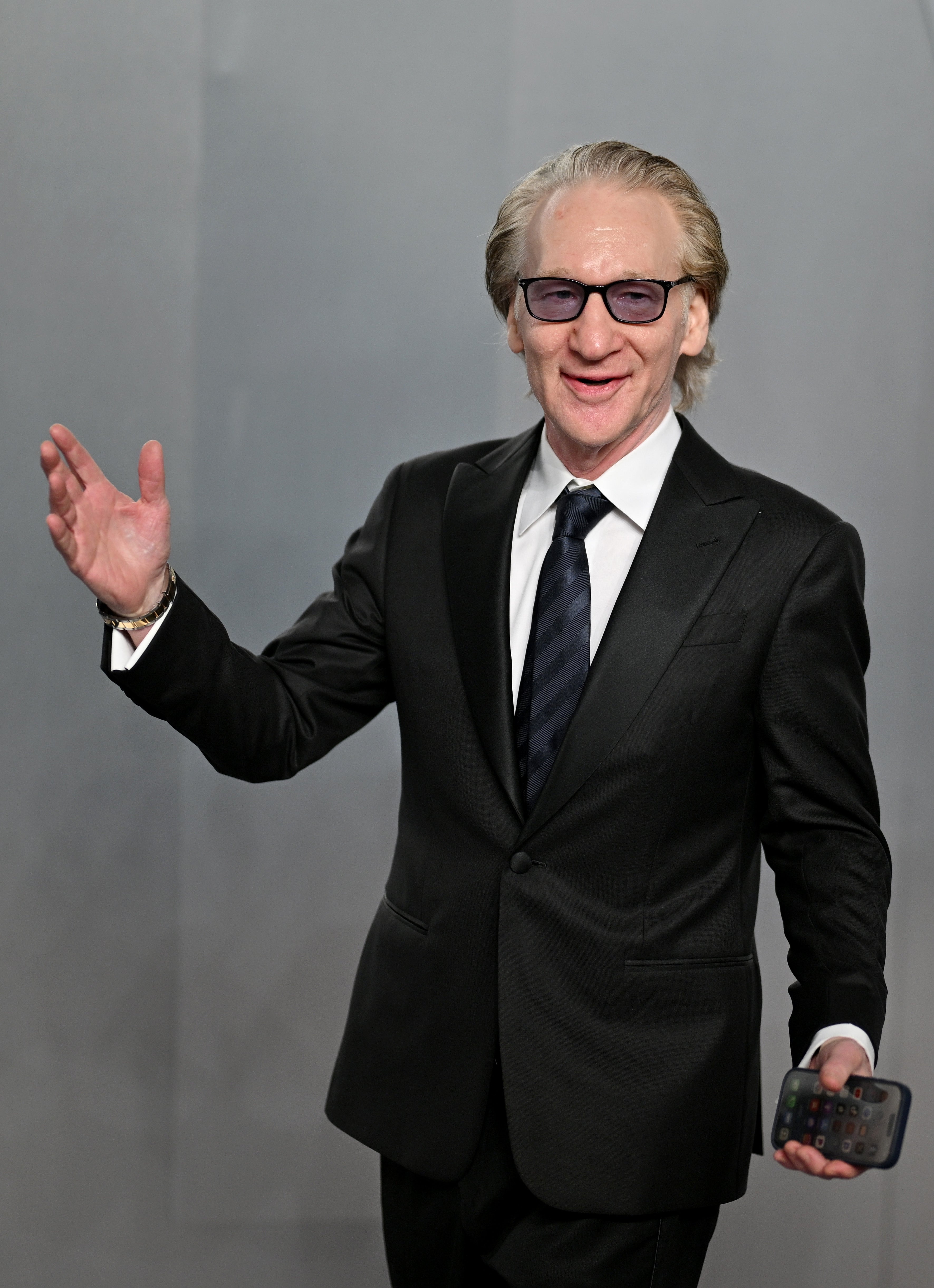Person successful  a sleek suit   smiling and holding a phone, gesturing with unfastened  arms connected  a neutral background