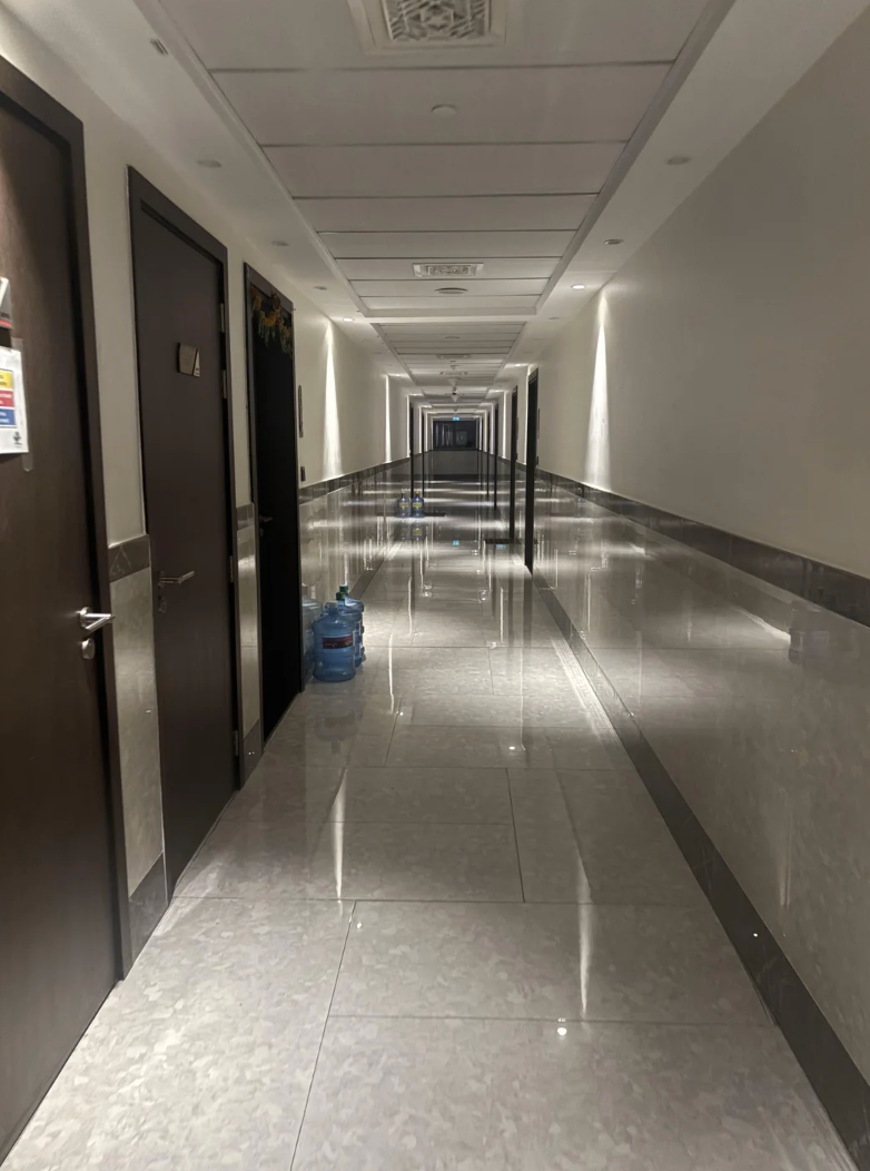 A long, empty corridor with polished floors and closed doors on either side, with a water dispenser placed near a door on the left