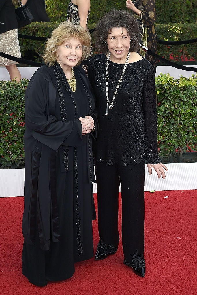 Two individuals connected a reddish carpet; 1 successful a long, flowing outfit, the different successful a sleek, sparkling ensemble, some smiling astatine the event