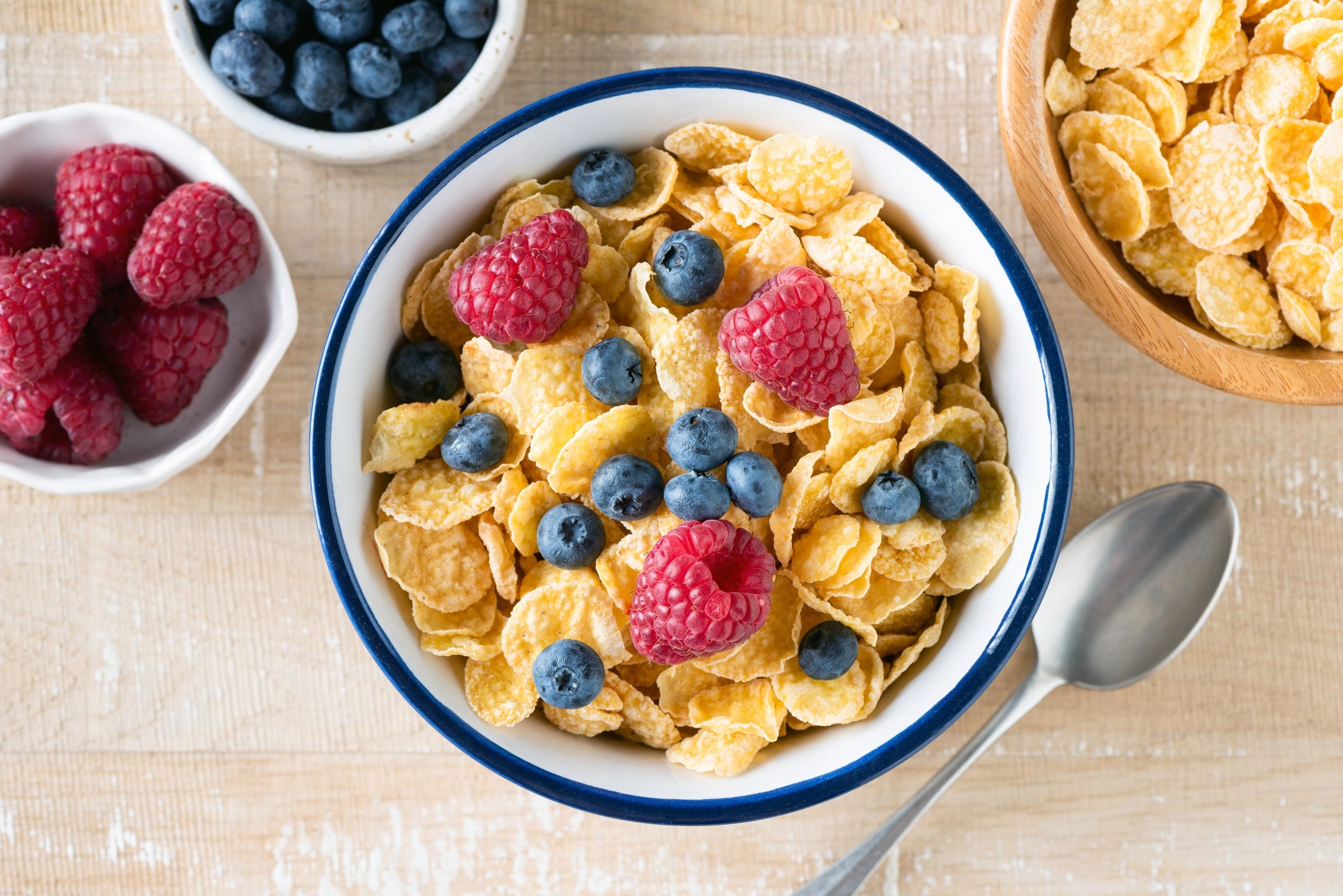 Bowl of cornflakes topped with raspberries and blueberries, with other berries successful bowls nearby, and a spoon connected the side