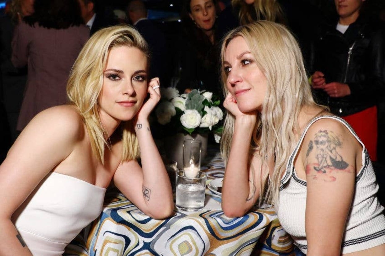 Two people at a table with a floral centerpiece, one in a strapless top and the other in a sleeveless top with a tattoo
