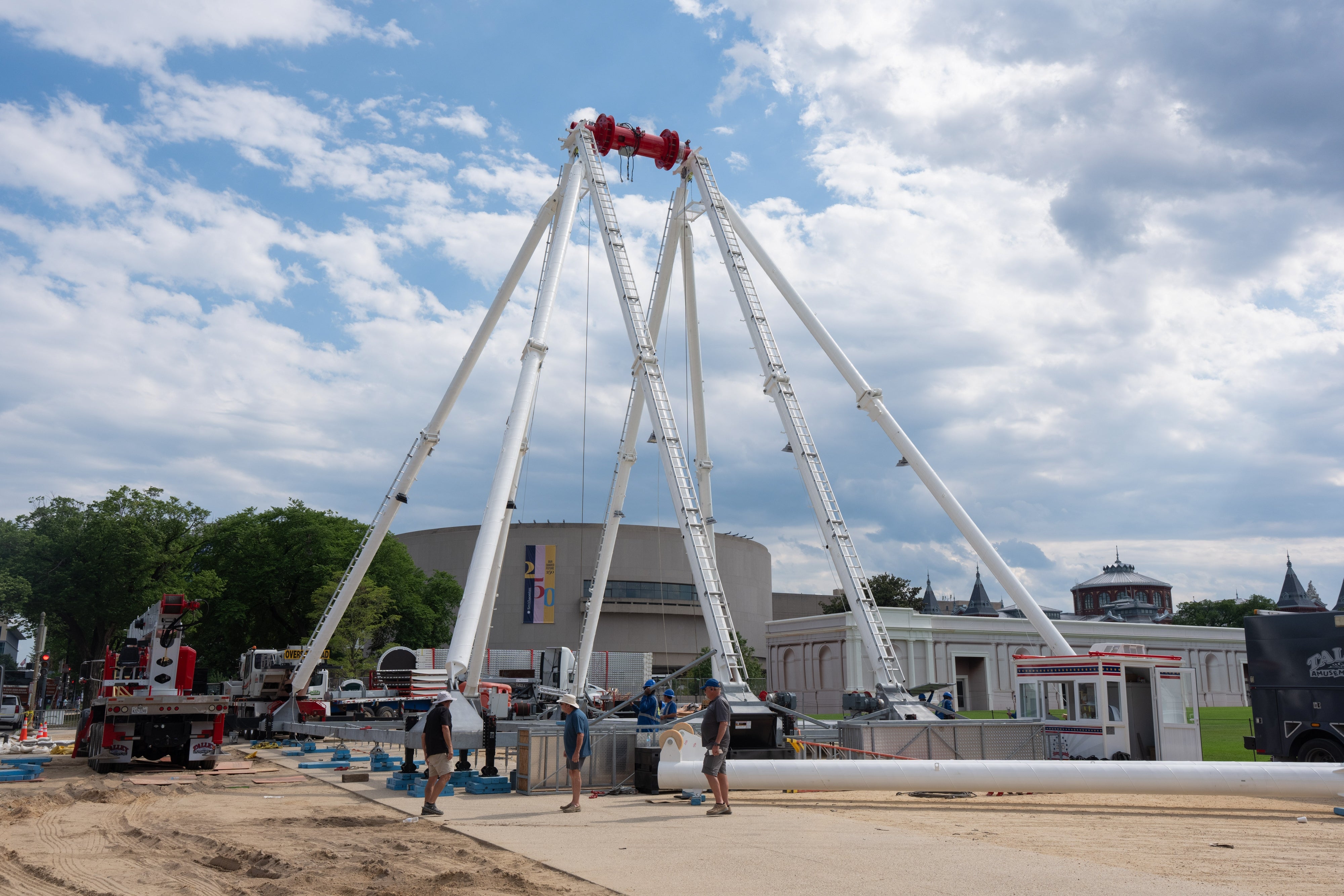 Ferris instrumentality installation astatine a fairground successful progress, workers preparing the operation with machinery and tools, nether a partially cloudy sky