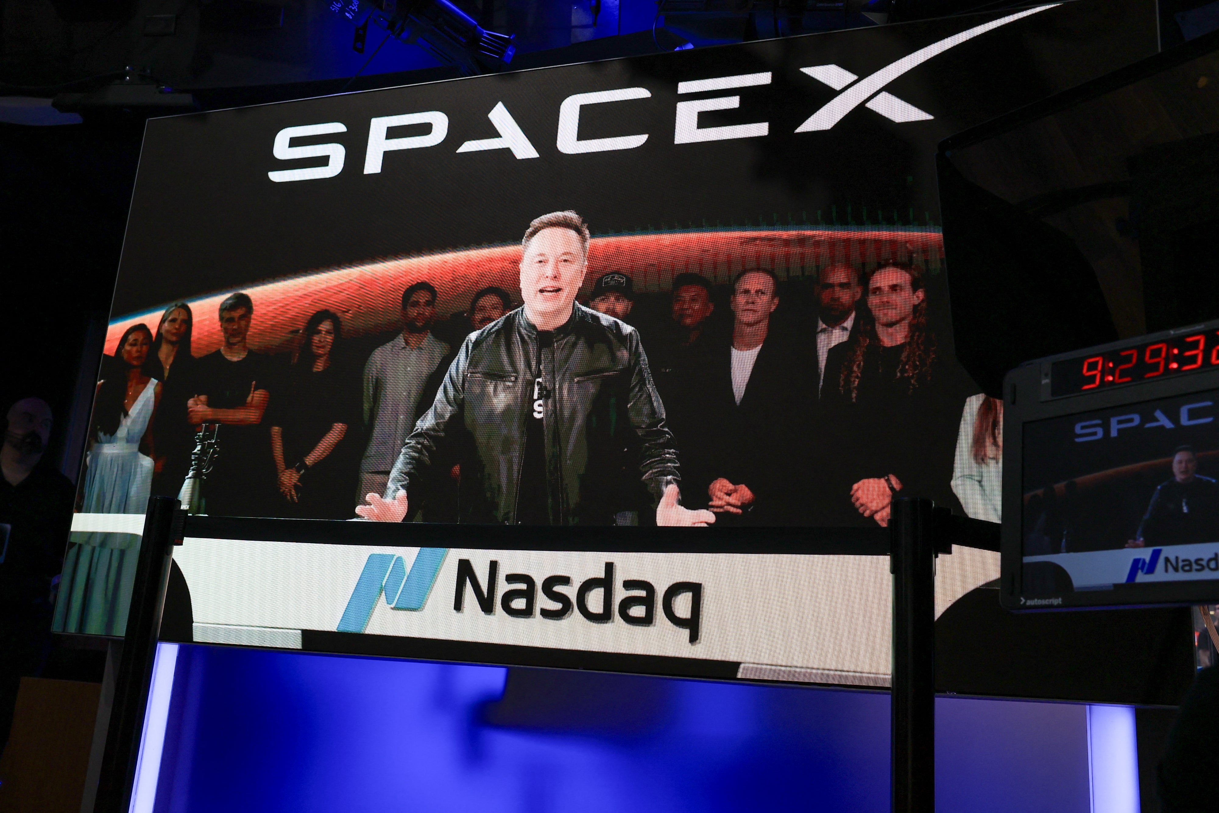 Man successful a leather overgarment speaks astatine an lawsuit with radical down him and "SpaceX" and "Nasdaq" logos visible