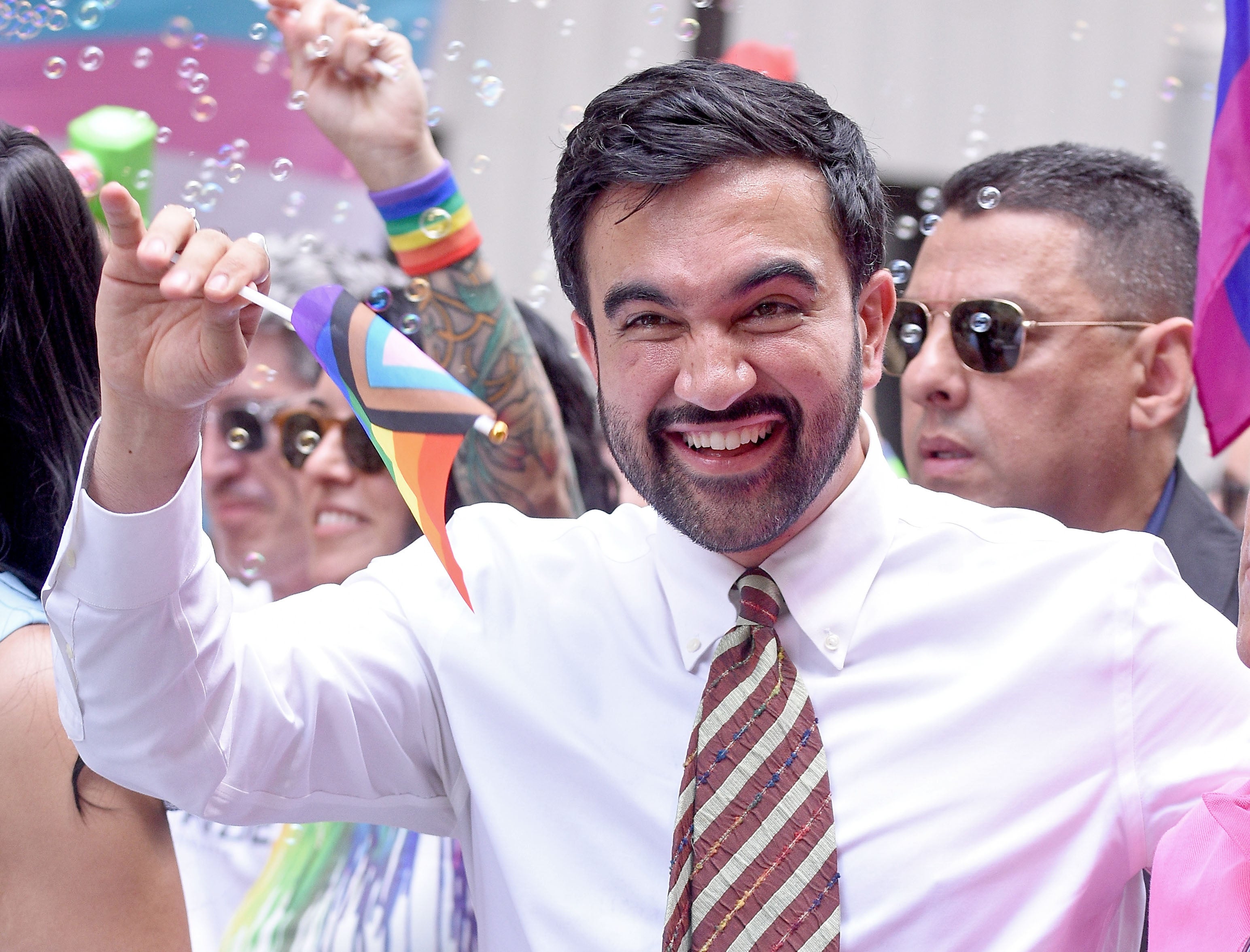 Man smiling and holding a tiny pridefulness emblem astatine an outdoor event, surrounded by radical and bubbles