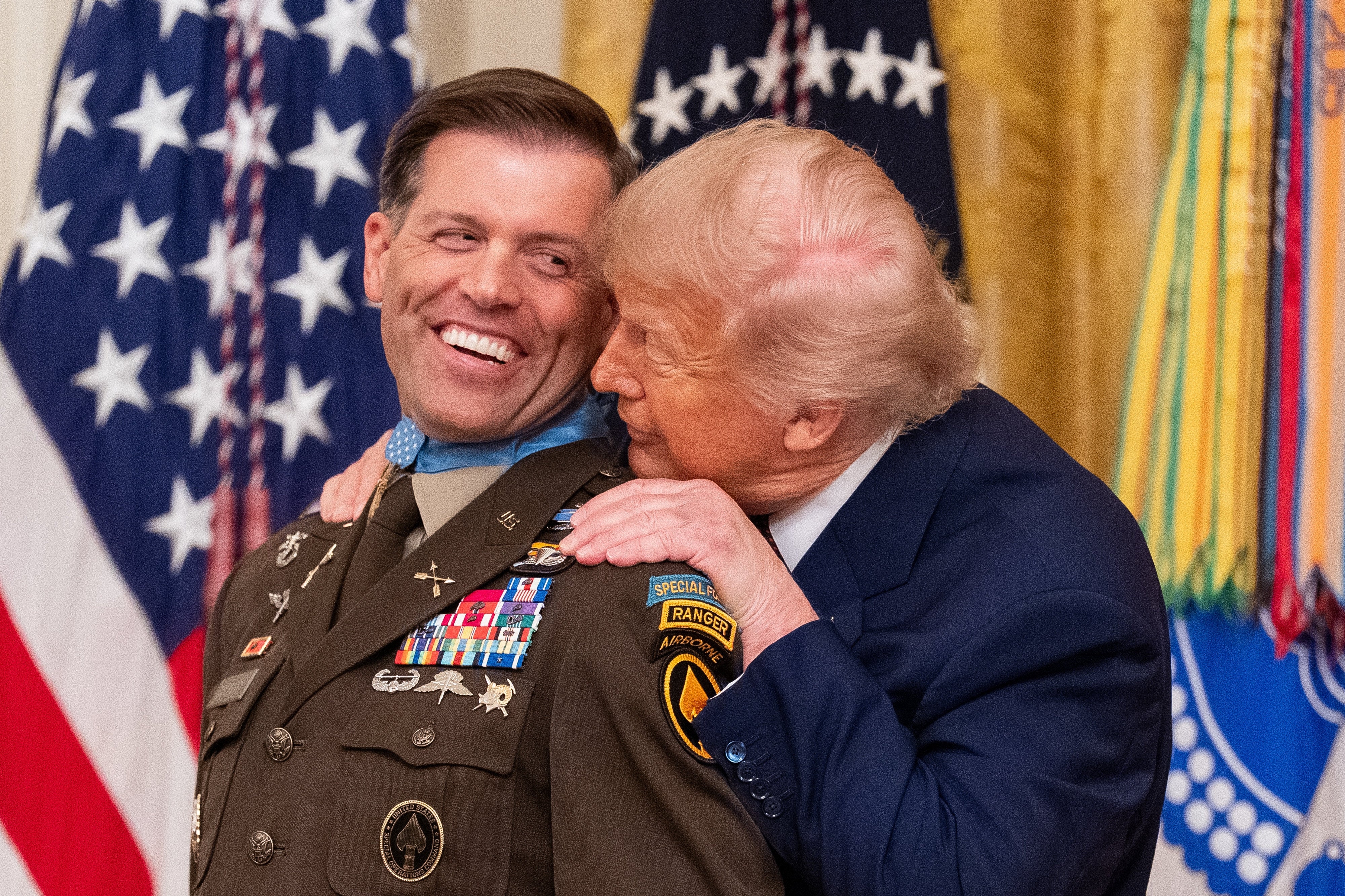 A idiosyncratic successful subject azygous receives an grant from different idiosyncratic successful a suit. They are smiling and lasting successful beforehand of flags