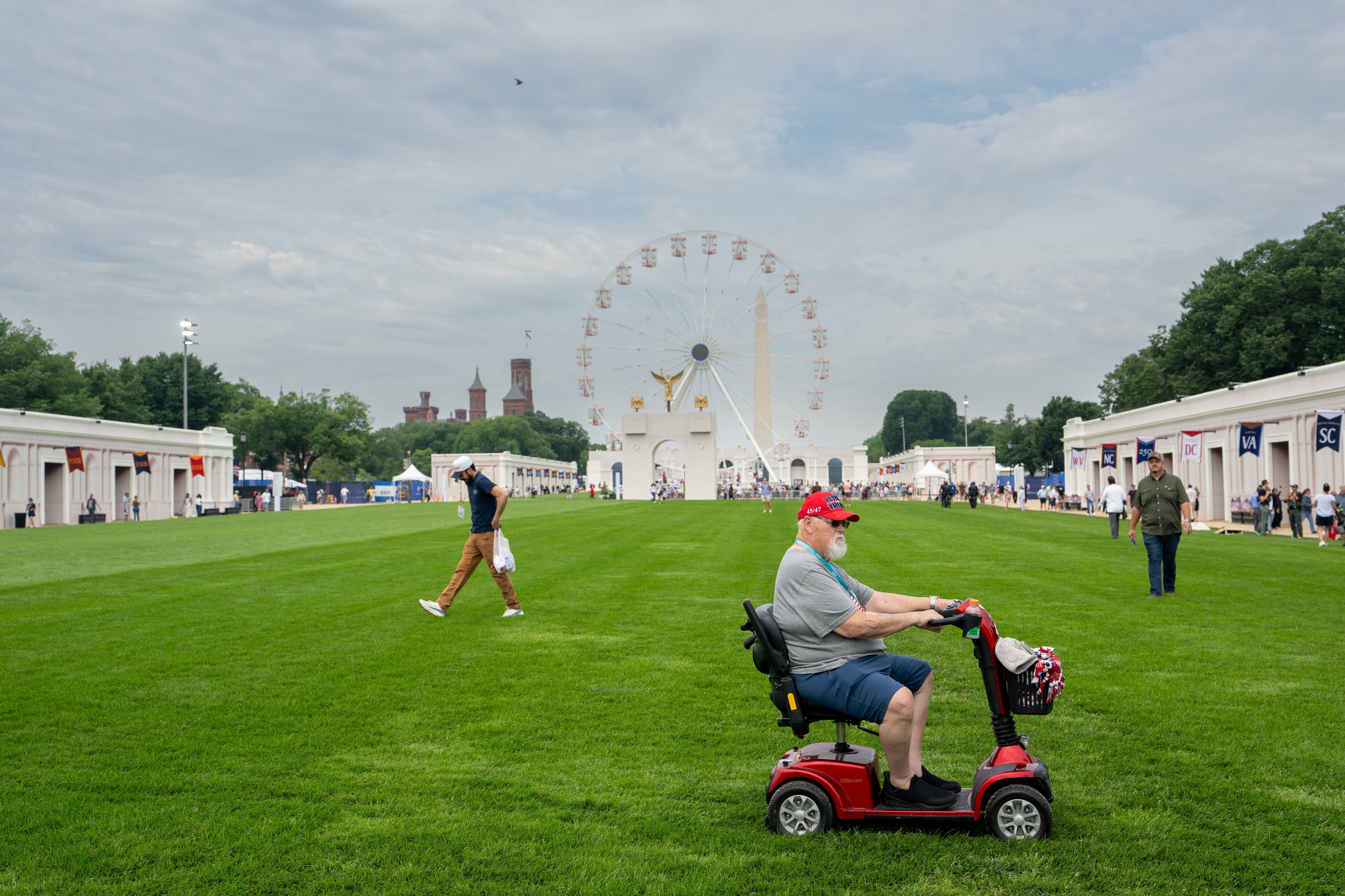A antheral wearing a headdress rides a mobility scooter connected a grassy tract with a Ferris instrumentality successful the background