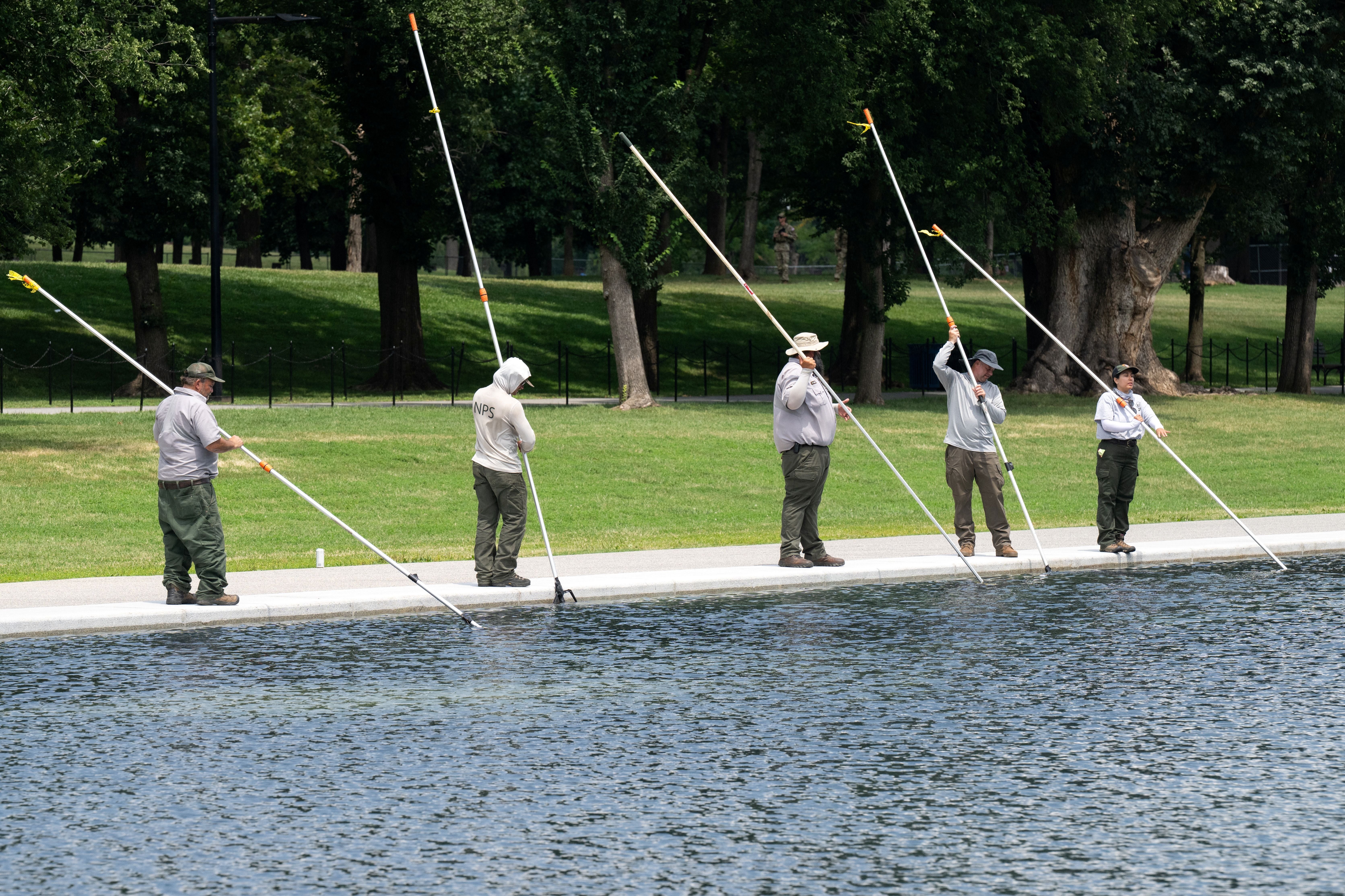People cleanable a reflecting excavation utilizing agelong poles, lasting successful a enactment on the pool's borderline successful a park