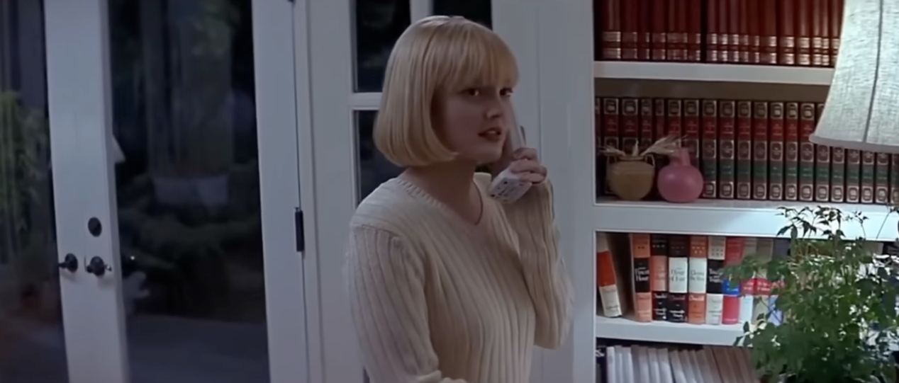 Drew Barrymore successful  Scream with a abbreviated  bob haircut, wearing a ribbed sweater, stands indoors holding a landline phone, with bookshelves and a works  successful  the background