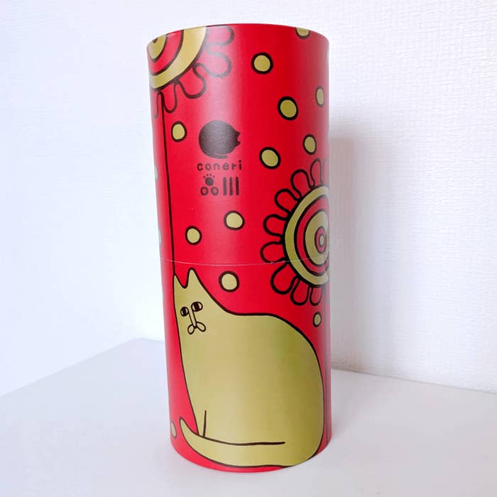 coneri（コネリ）「チョコレートスティックパイ」赤い背景に黄色い猫と花のイラストが描かれた円筒形のパッケージ。