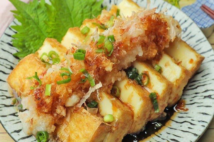 皿に盛られた揚げ出し豆腐、かつお節とネギ、白味がかかったソース添え。