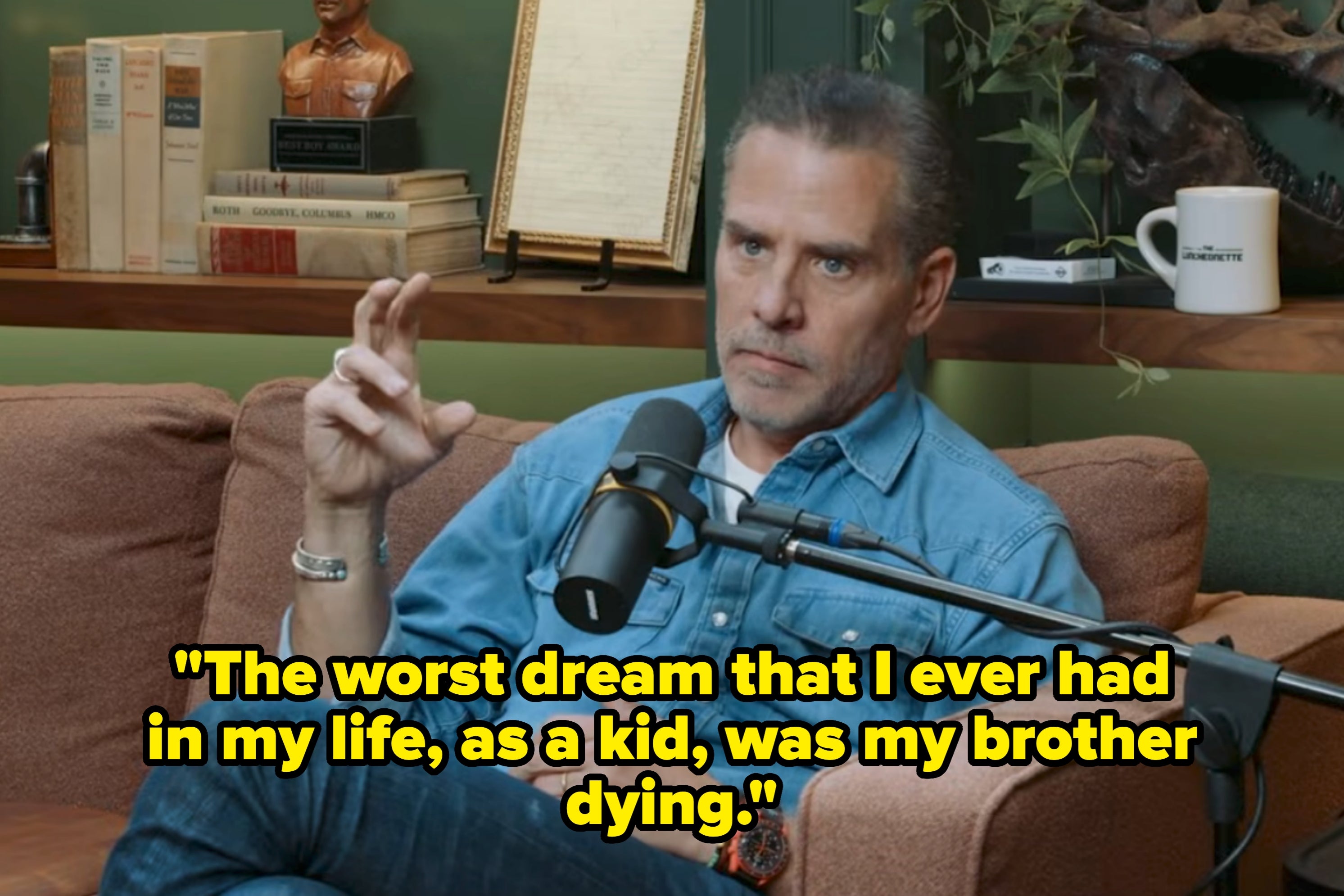 Man in denim shirt speaking into a microphone, seated on a sofa, discussing a past fear of his brother dying