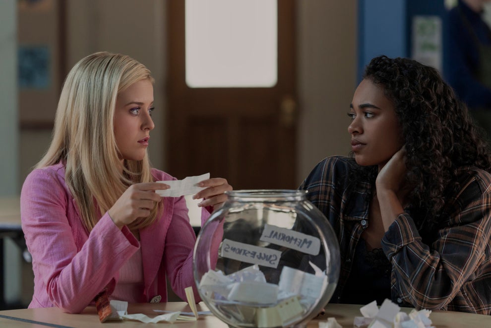 Two people sit at a table with a clear bowl full of paper slips, engaged in conversation