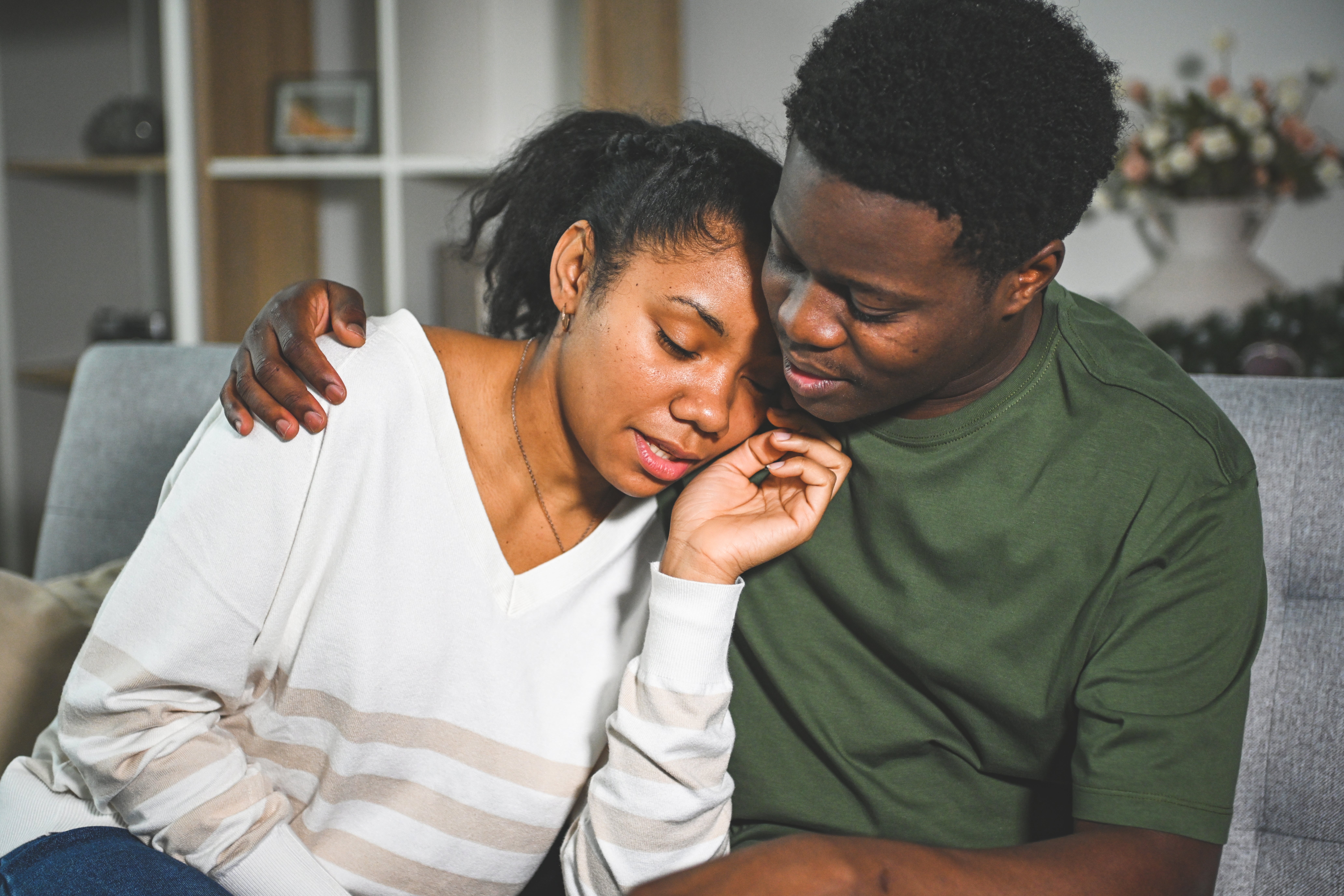 A couple sits closely on a sofa, embracing tenderly, conveying love and comfort